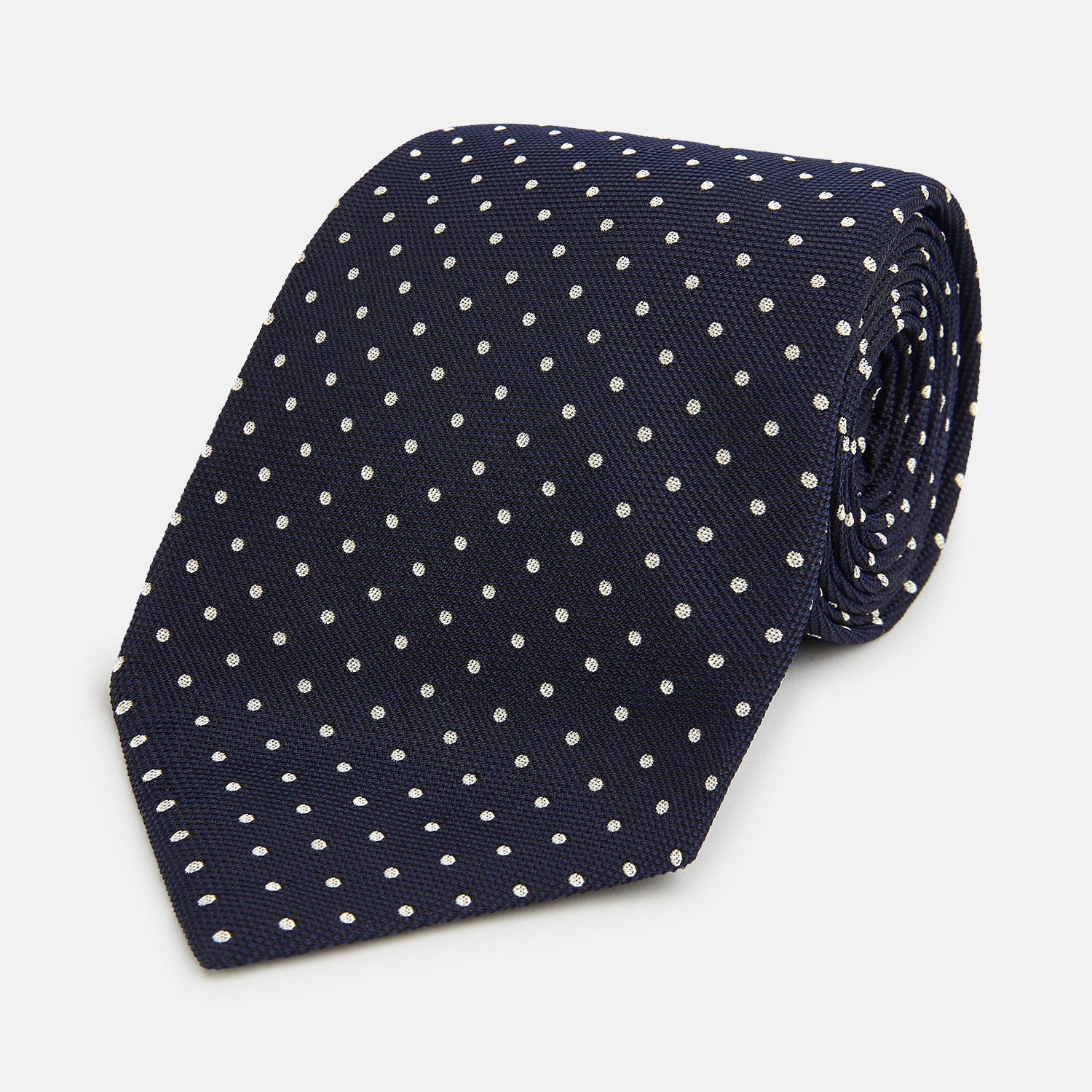 Image 1 of product The Silver and Navy Micro Dot Silk Tie by Turnbull & Asser features a refined micro dot pattern, perfect for adding a classic accent to formal attire. Shown neatly rolled on a white background.