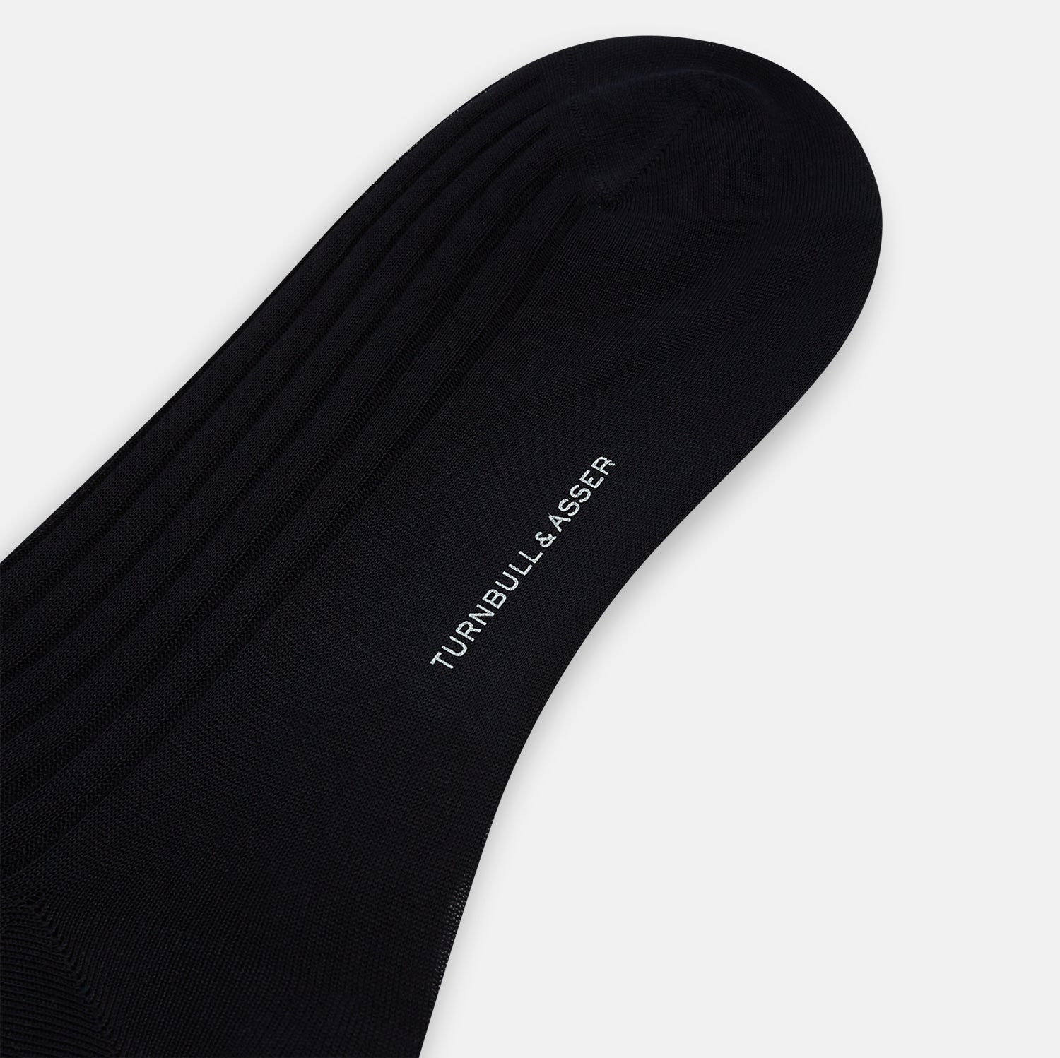 Image 3 of product A single Midnight Mid-length Sock by Turnbull & Asser, made from mercerised Egyptian cotton, stands upright on a white background. This luxury black sock features a ribbed texture with smooth toe and heel areas.
