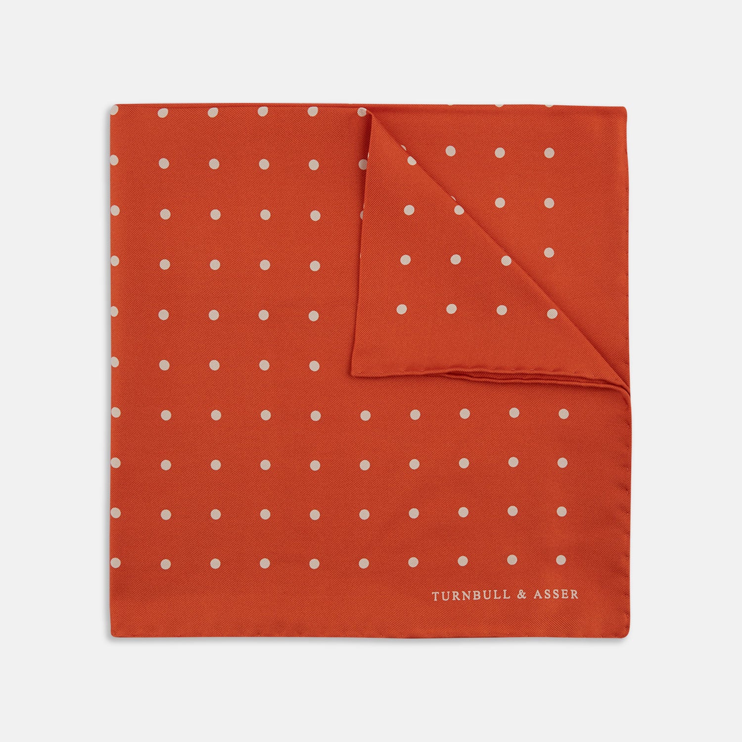Image 1 of product The Orange Spot Silk Pocket Square by Turnbull & Asser features evenly spaced white polka dots and the brand’s name in one corner, making this dapper accessory a standout addition to any outfit.