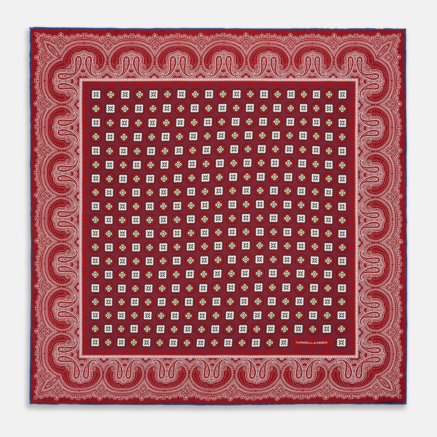 Image 9 of product The Turnbull & Asser Red Floral Tile and Paisley Silk Pocket Square features red silk with white and green paisley and geometric patterns, a blue border, a folded corner revealing both sides, branding in white, and is handcrafted in England.