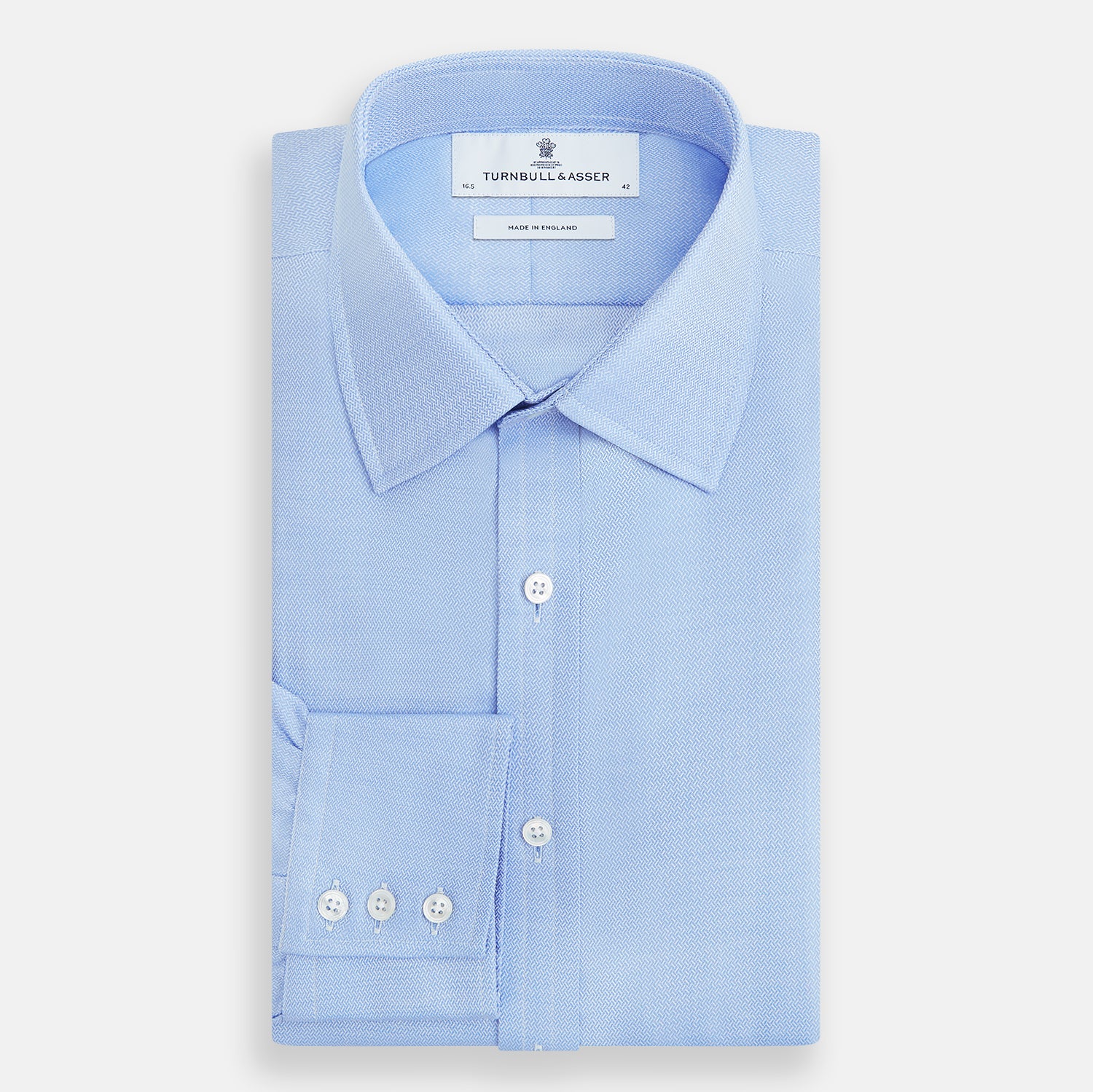 Image 5 of product The Blue Herringbone Mayfair Shirt by Turnbull & Asser features light blue and white stripes, long sleeves, a classic collar, white buttons, and buttoned cuffs. Shown on a plain white background, it's perfect for formal occasions.