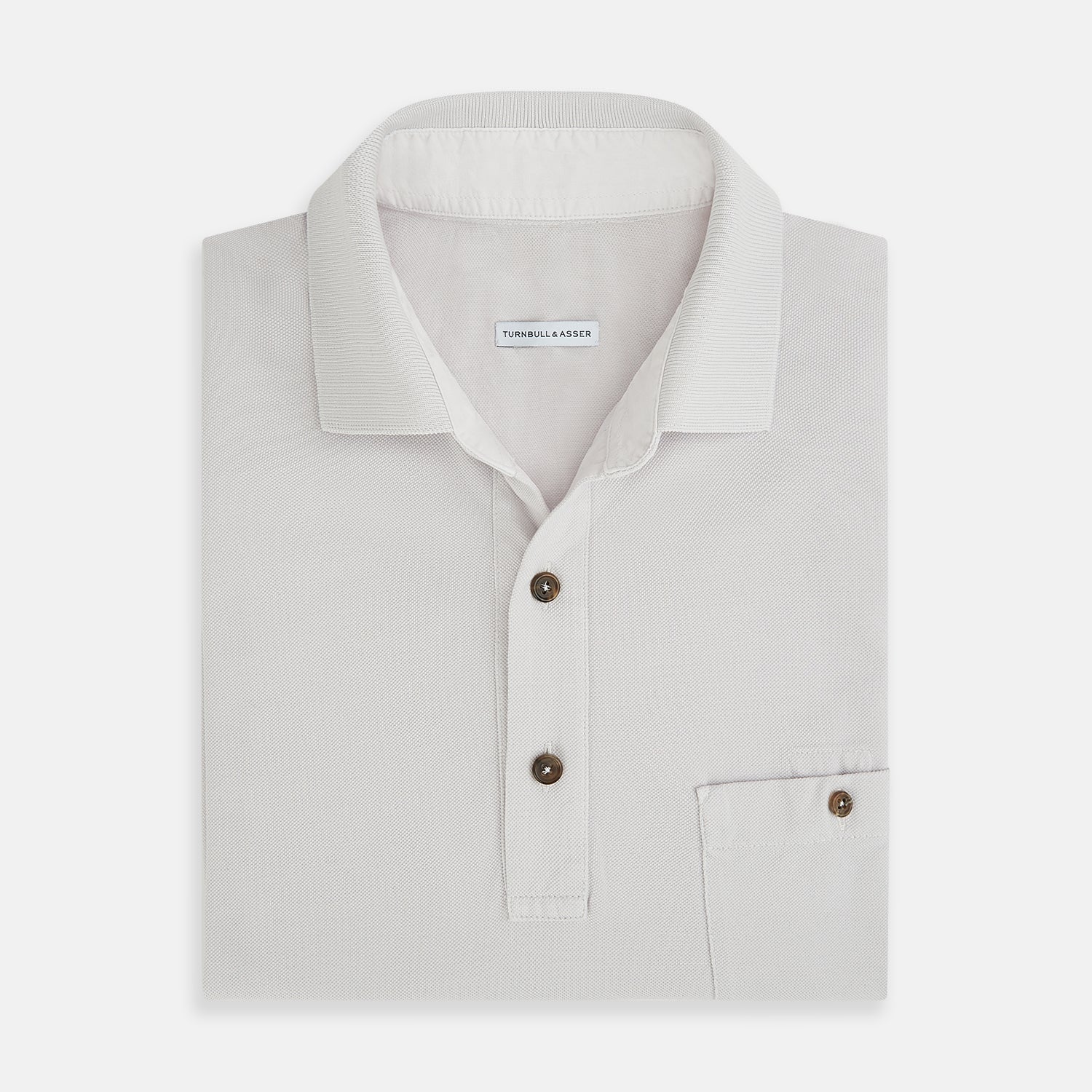 Image 4 of product The Turnbull & Asser Pale Pink Polo Shirt is a cotton jersey short-sleeve polo with a collar, three brown buttons on the placket, and a button-flap chest pocket, shown against a white background.