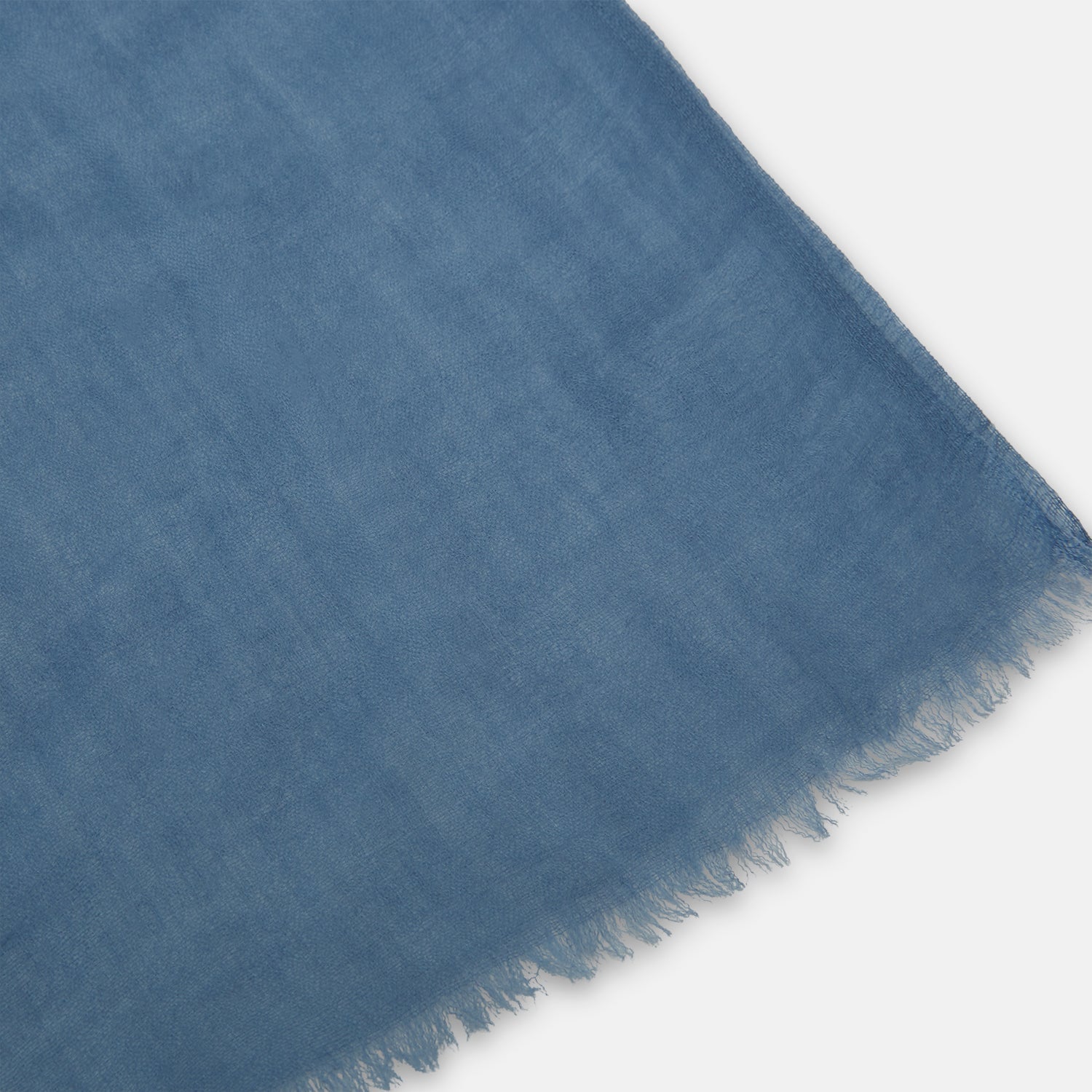 Image 2 of product The Turnbull & Asser Mid Blue Cashmere Scarf is lightweight and slightly sheer, hand-dyed with frayed ends, shown loosely knotted against a white background.