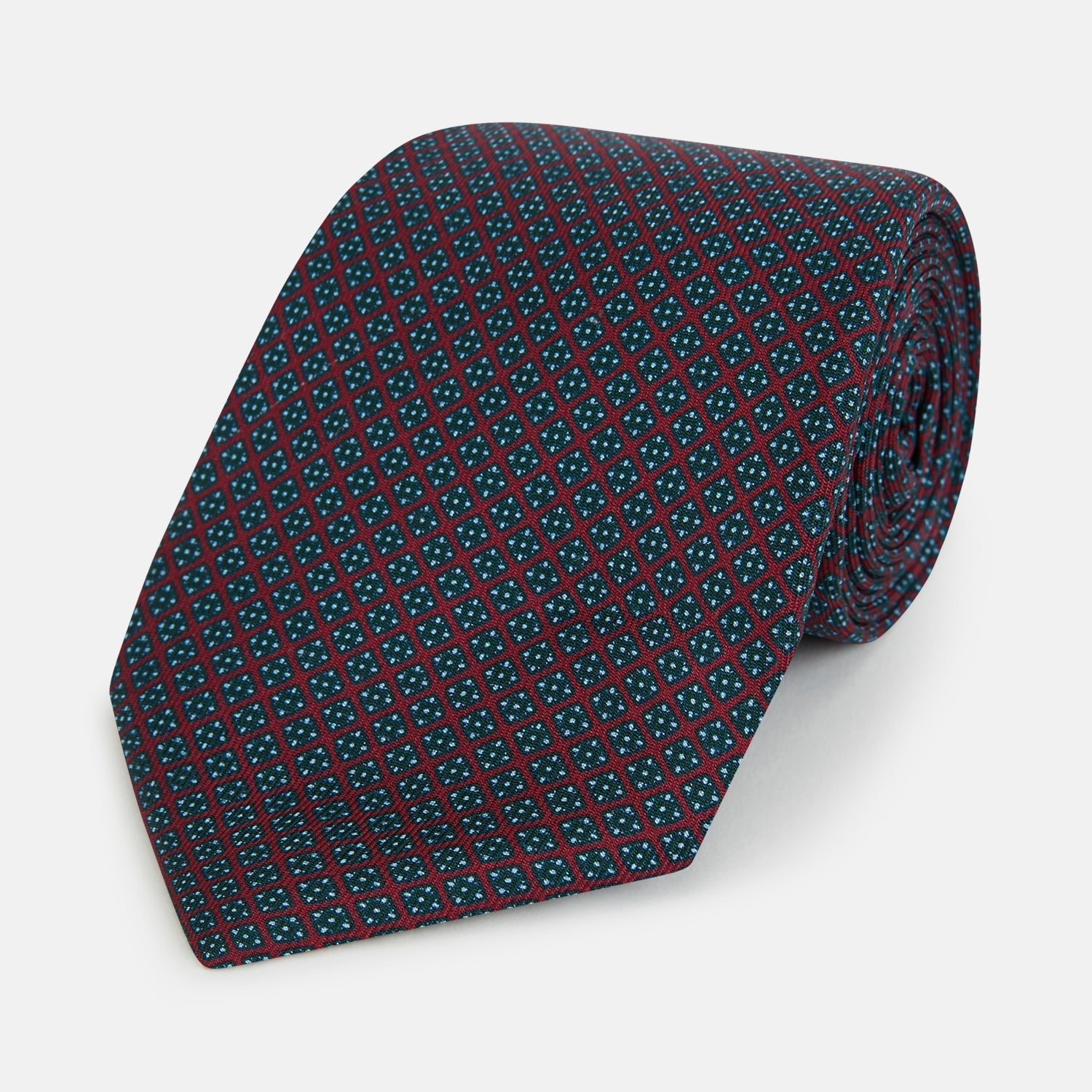 Image 1 of product The Turnbull & Asser Magenta and Navy Square-Patterned Silk Tie is neatly rolled on a plain light background.