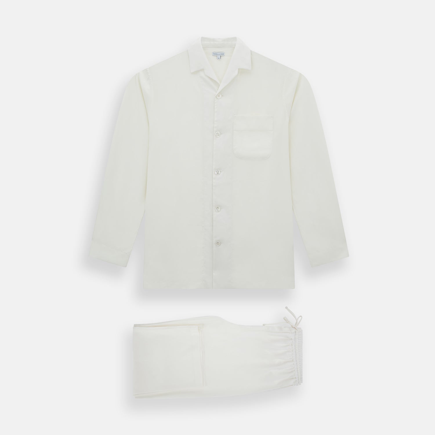 Image 1 of product The Turnbull & Asser Cream Silk Pyjama Set, shown laid flat on a white background, features a long-sleeve button-up top with a chest pocket and matching pants with an elastic drawstring waist—ideal for comfortable loungewear.