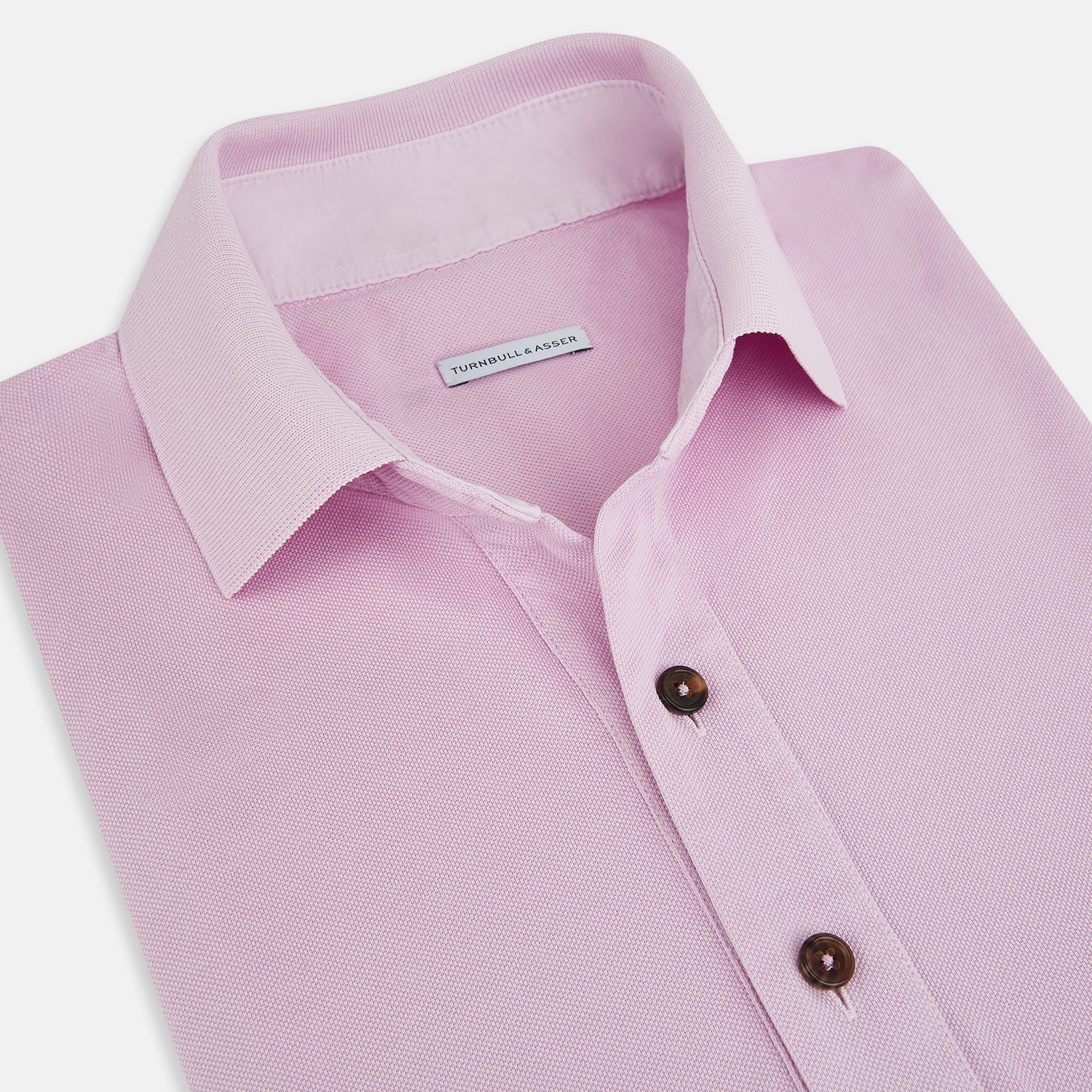 Image 2 of product The Turnbull & Asser Pink Polo Shirt is a men's cotton polo with short sleeves, a collar, three dark buttons, and a chest pocket with a button, shown laid flat on a white background.