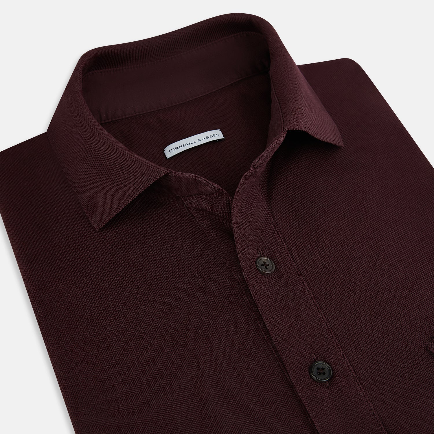 Image 2 of product The Turnbull & Asser Burgundy Polo Shirt is crafted from soft cotton jersey with short sleeves, a classic collar, three front buttons, and a small buttoned chest pocket, shown flat on a white background.