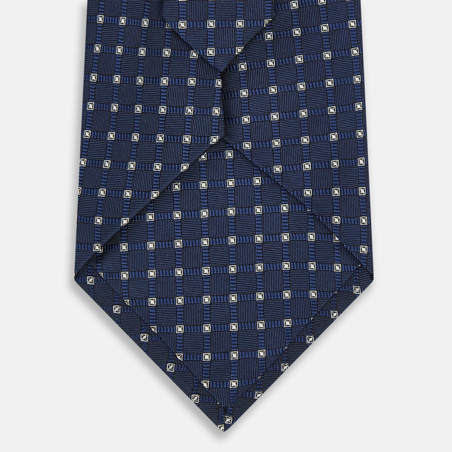 Image 3 of product The Turnbull & Asser Navy and White Geometric Silk Tie, featuring a micro pattern of light blue and white squares, is displayed rolled up on a plain white background.