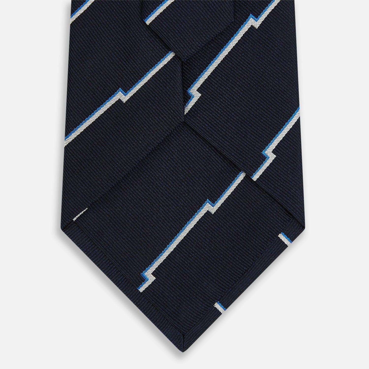 Image 3 of product The Turnbull & Asser Navy Broken Shadow Stripe Silk Tie features British excellence with a light blue and white zigzag pattern and is shown rolled up on a plain white background.