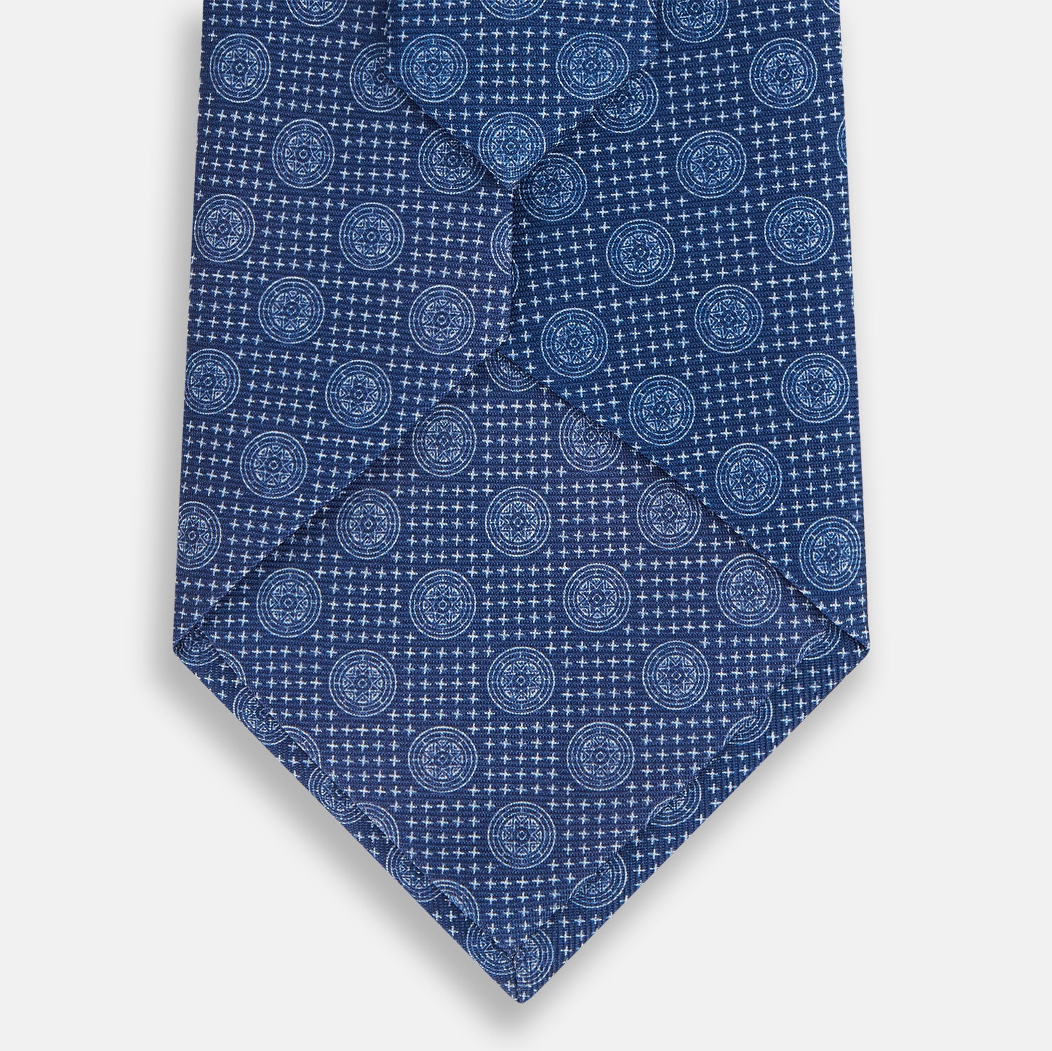 Image 3 of product The Turnbull & Asser Azzurro Medallion Silk Tie, rolled up and displayed on a white background, features small geometric medallion motifs in lighter blue tones.