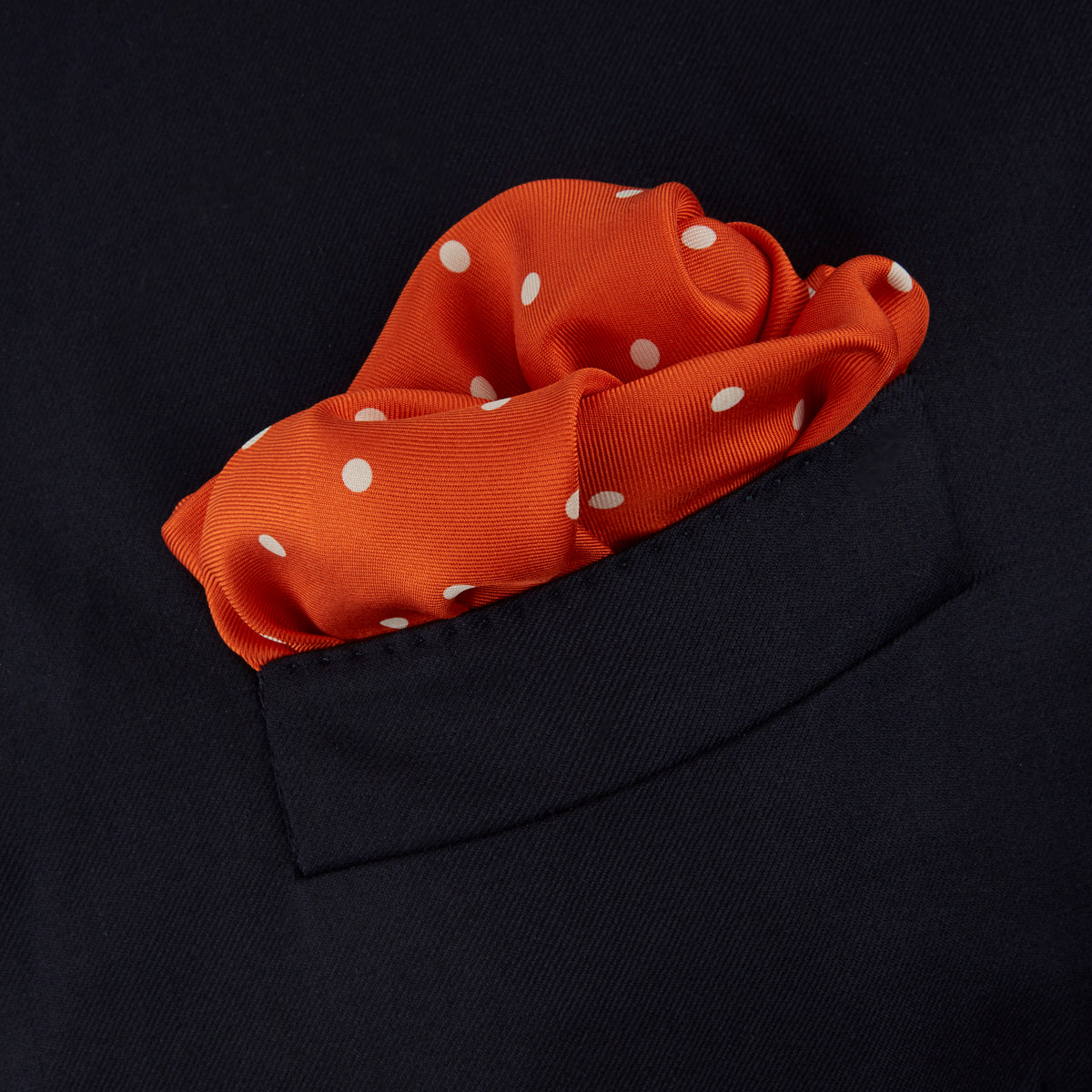 Image 4 of product The Orange Spot Silk Pocket Square by Turnbull & Asser features evenly spaced white polka dots and the brand’s name in one corner, making this dapper accessory a standout addition to any outfit.
