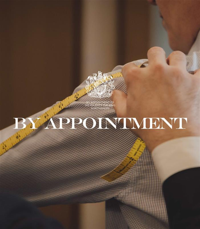 A tailor measures a person’s arm with a yellow measuring tape. The words “BY APPOINTMENT” and a royal crest overlay the image.
