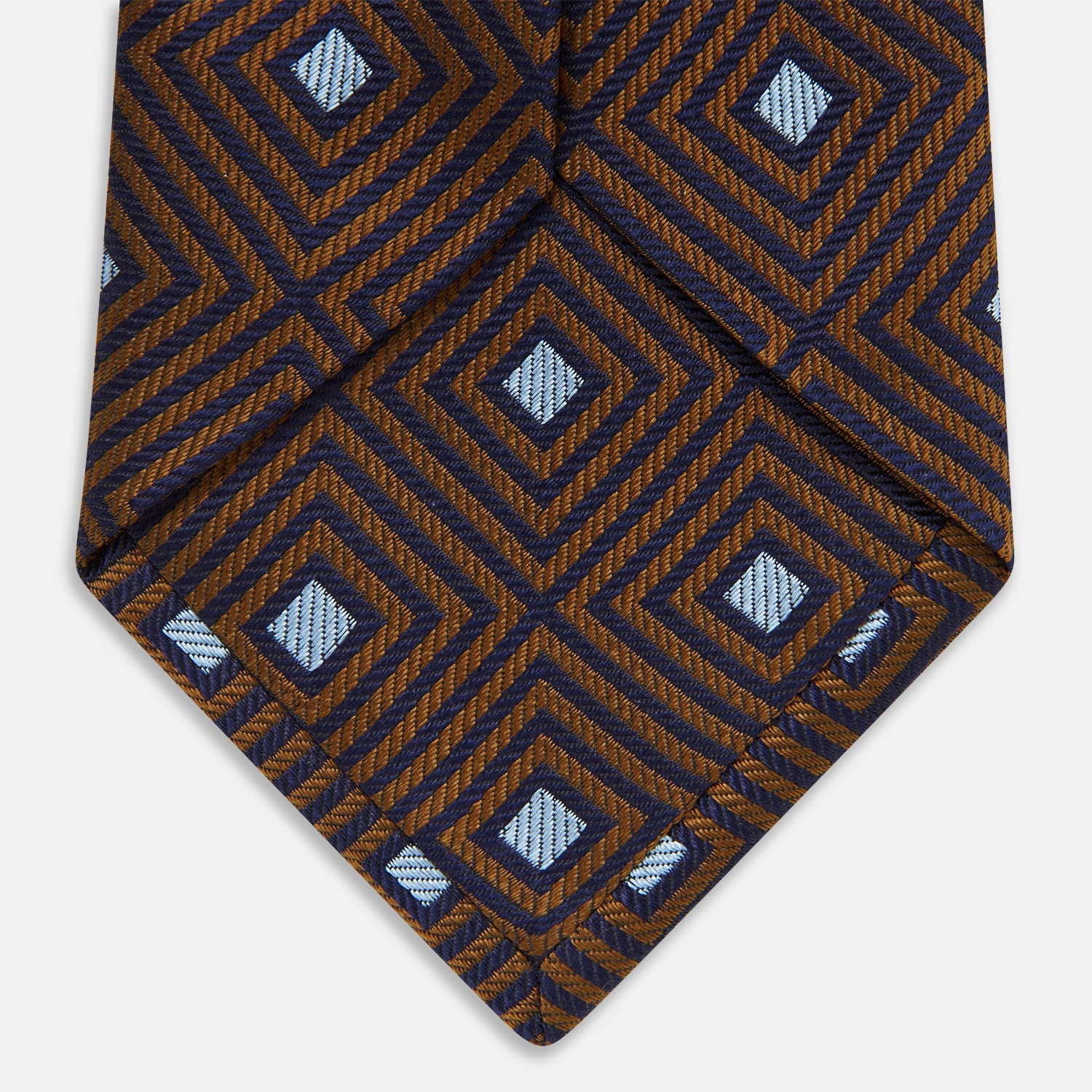 Image 5 of product The Tomorrow Never Dies Square Silk Tie by Turnbull & Asser, as seen on James Bond, features a brown and blue geometric diamond pattern on a dark background—an ideal accessory for any Bond-inspired look. Displayed rolled on a plain white surface.