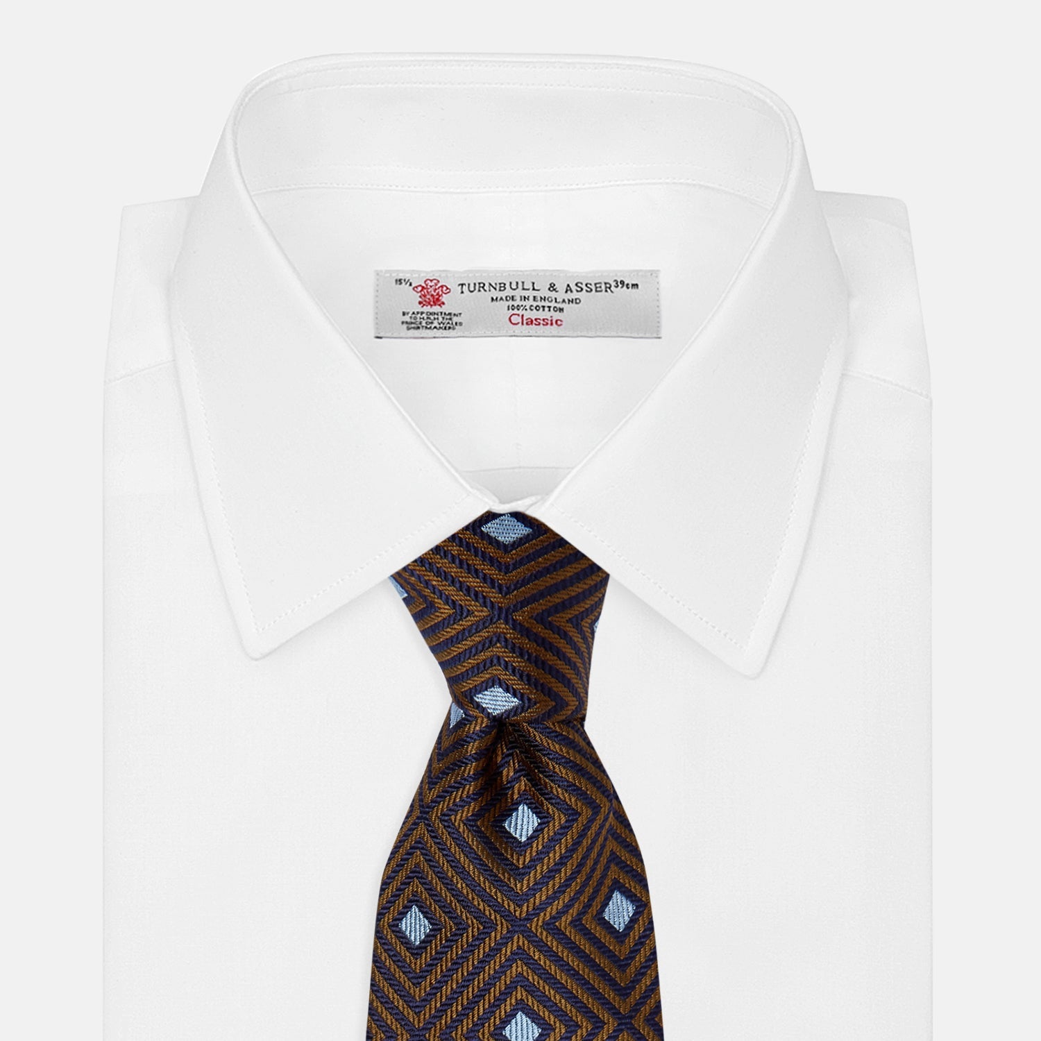 Image 3 of product The Tomorrow Never Dies Square Silk Tie by Turnbull & Asser, as seen on James Bond, features a brown and blue geometric diamond pattern on a dark background—an ideal accessory for any Bond-inspired look. Displayed rolled on a plain white surface.