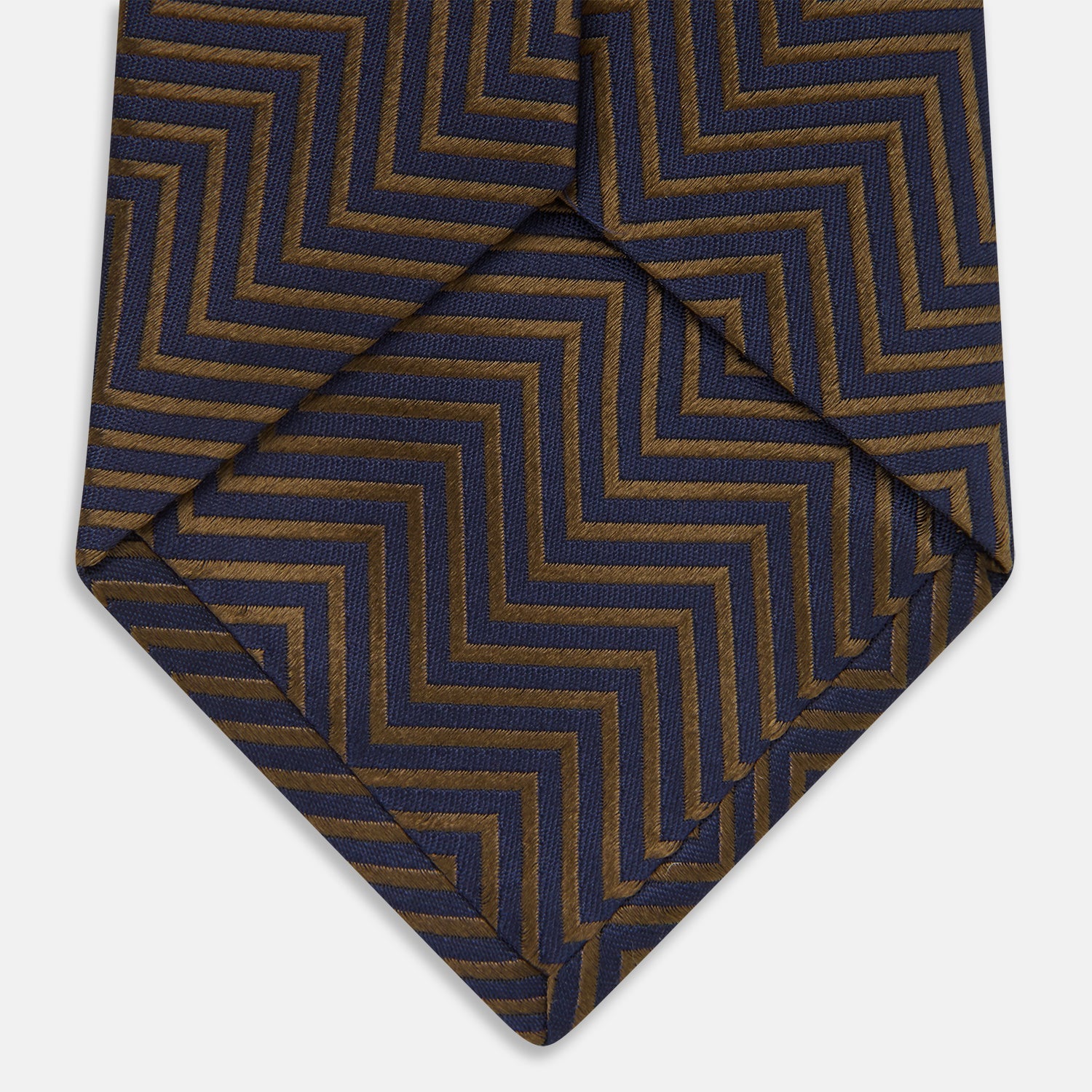 Image 5 of product Turnbull & Asser's "The World Is Not Enough" Zig Zag Silk Tie, as seen on James Bond, features a bold navy blue and gold chevron design and is shown neatly rolled on a white background.