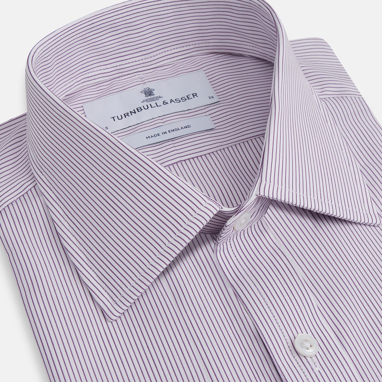 Image 2 of product The Purple Pinstripe Mayfair Shirt by Turnbull & Asser is a light purple cotton poplin long-sleeve button-up with white stripes, a pointed collar, white buttons, and cuffed sleeves, shown laid flat on a white background.