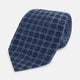 The Turnbull & Asser Navy Grid Silk Tie is handmade and neatly rolled, showcasing a dark blue silk fabric with a textured grid pattern, displayed on a plain white background.