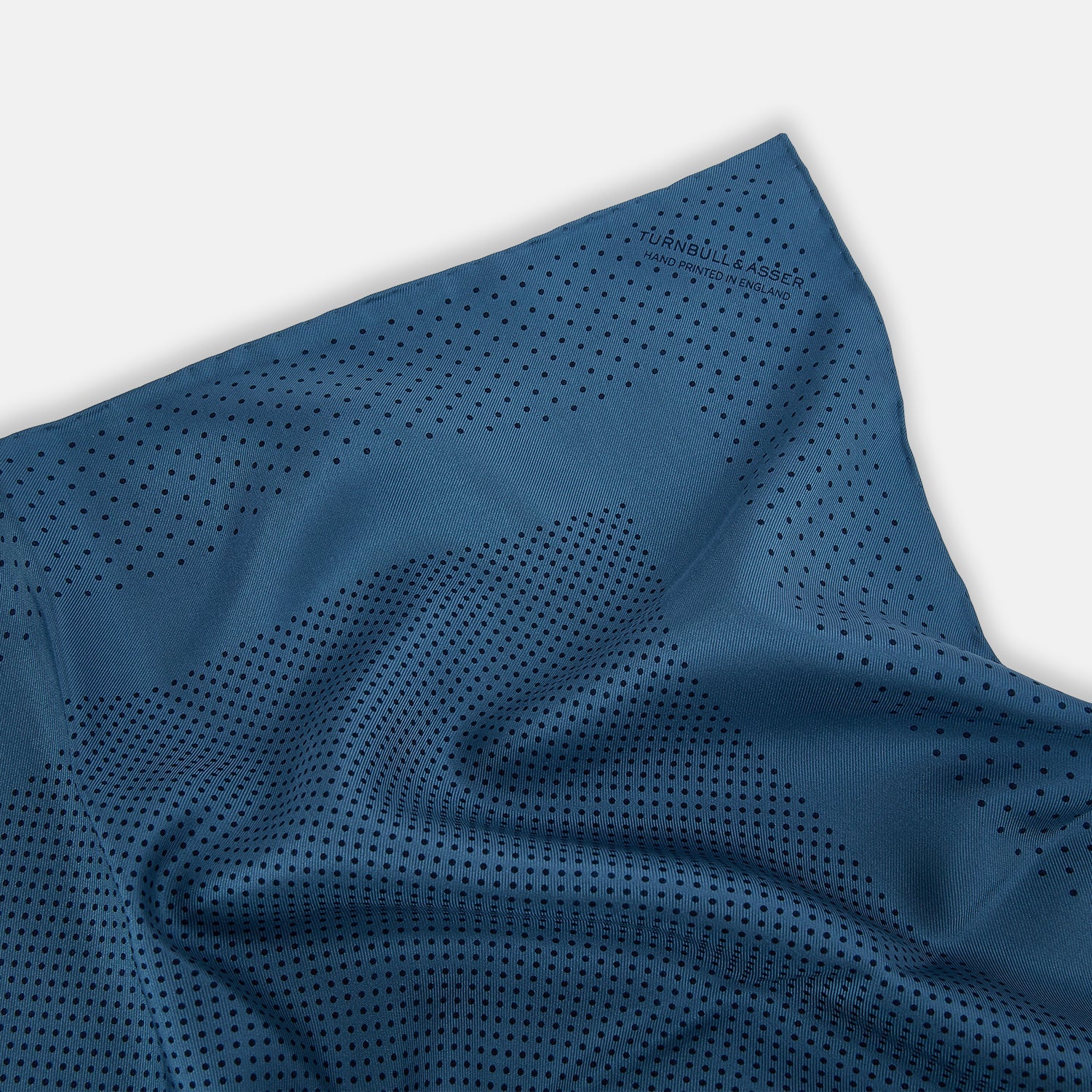 Image 2 of product The Blue Dot Silk Pocket Square by Turnbull & Asser features small black polka dots on blue silk and is made in England. The image shows it neatly folded, with a corner turned down to display both sides.
