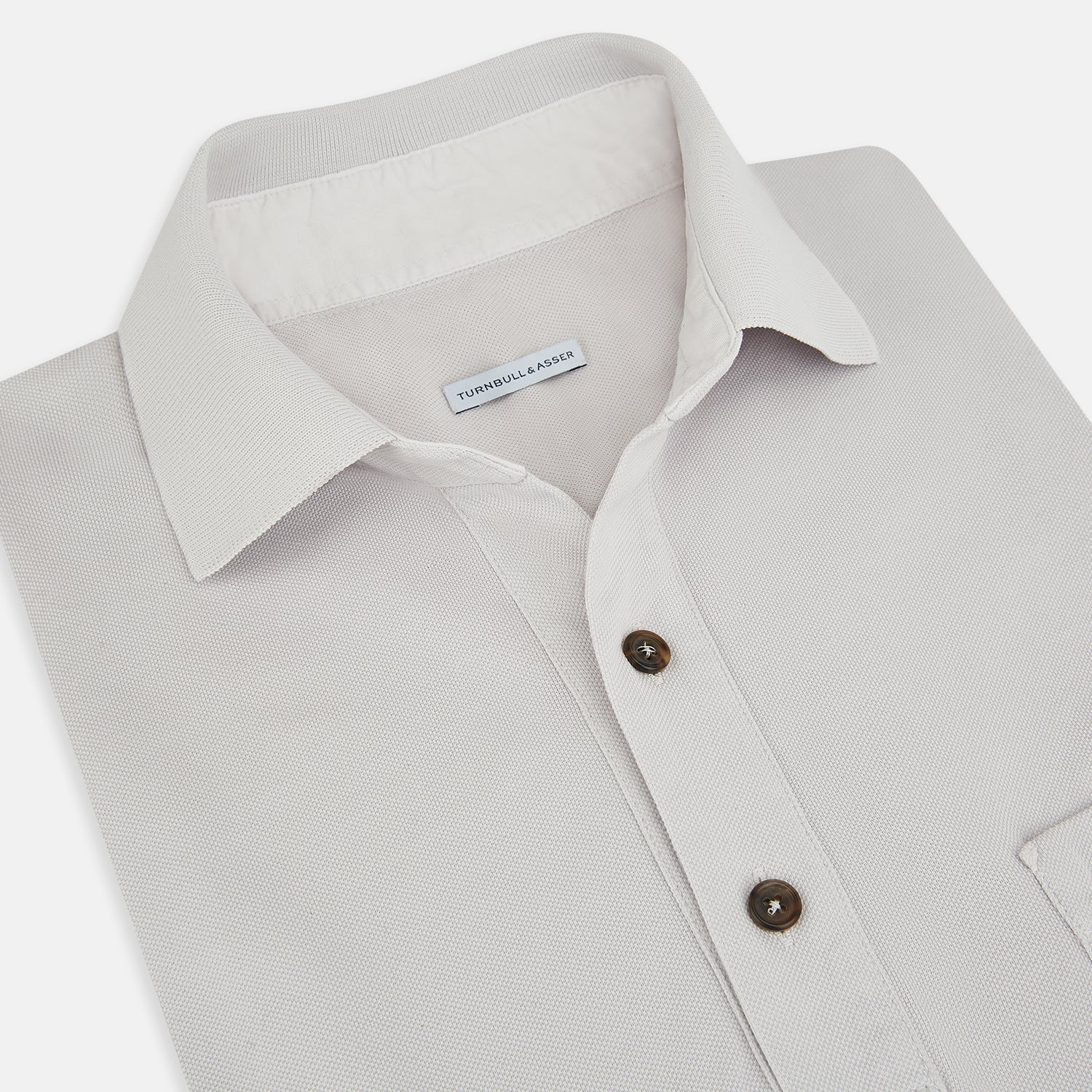 Image 2 of product The Turnbull & Asser Pale Pink Polo Shirt is a cotton jersey short-sleeve polo with a collar, three brown buttons on the placket, and a button-flap chest pocket, shown against a white background.