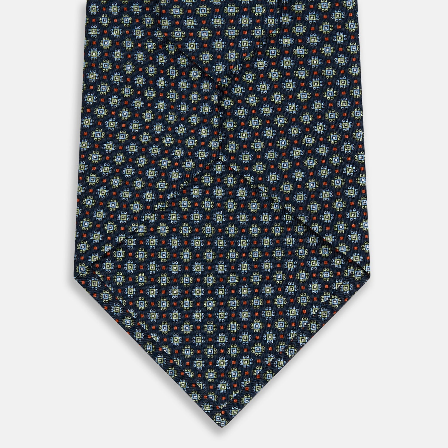 Image 3 of product The Turnbull & Asser Navy Geometric Floral Silk Tie features a dark blue background with a repeating small geometric pattern in light blue, yellow, and red, shown rolled up on a plain white surface.