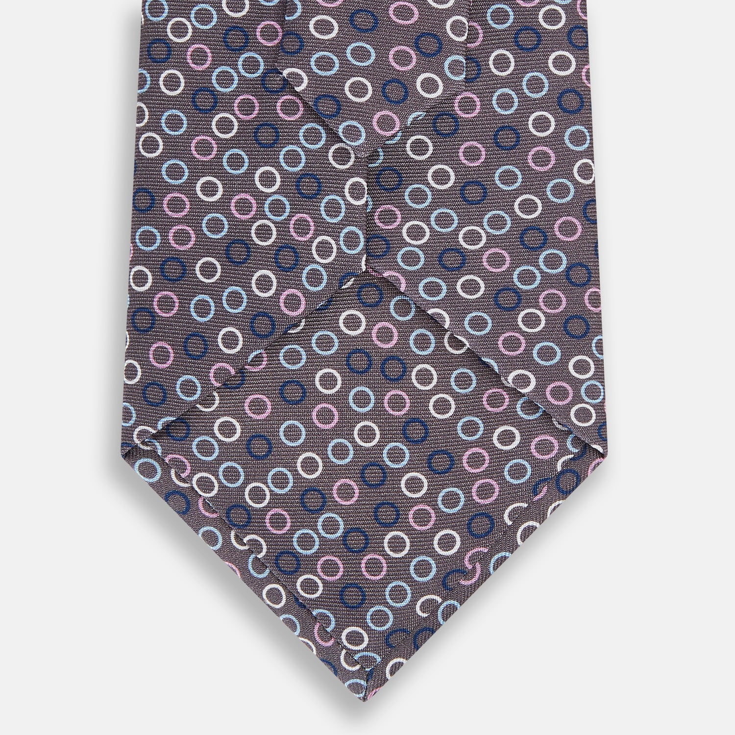 Image 3 of product The Turnbull & Asser Purple and Blue Circle Ash Silk Tie features small blue, pink, and white circles on a dark purple background, adding an elegant touch when displayed on a light surface.