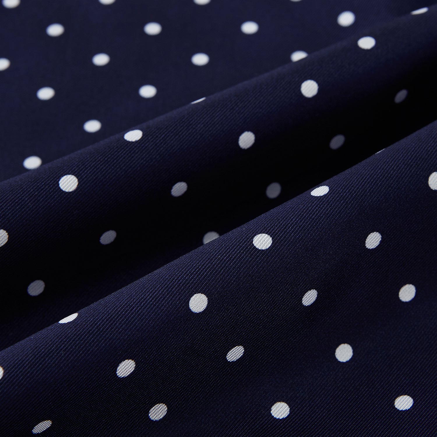 Image 3 of product The Navy and White Spotted Silk Scarf by Turnbull & Asser features white polka dots, a fringed edge, and the brand's name printed near the bottom on both sides. It is neatly folded at the top.