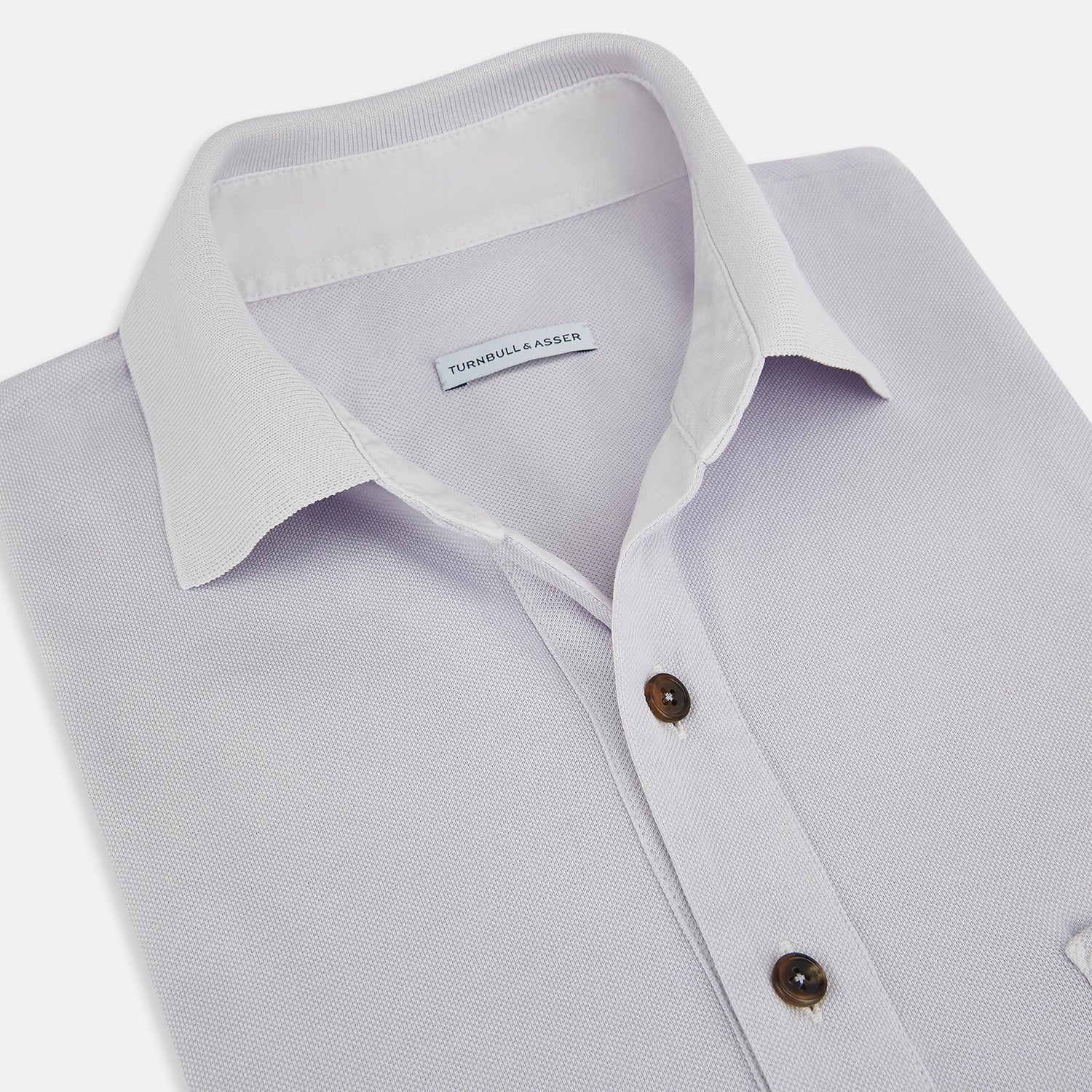 Image 2 of product A soft pink cotton polo shirt by Turnbull & Asser features short sleeves, a contrasting white collar, three dark buttons, and a left chest pocket. Laid flat on a white background—it’s perfect for modern men’s fashion.