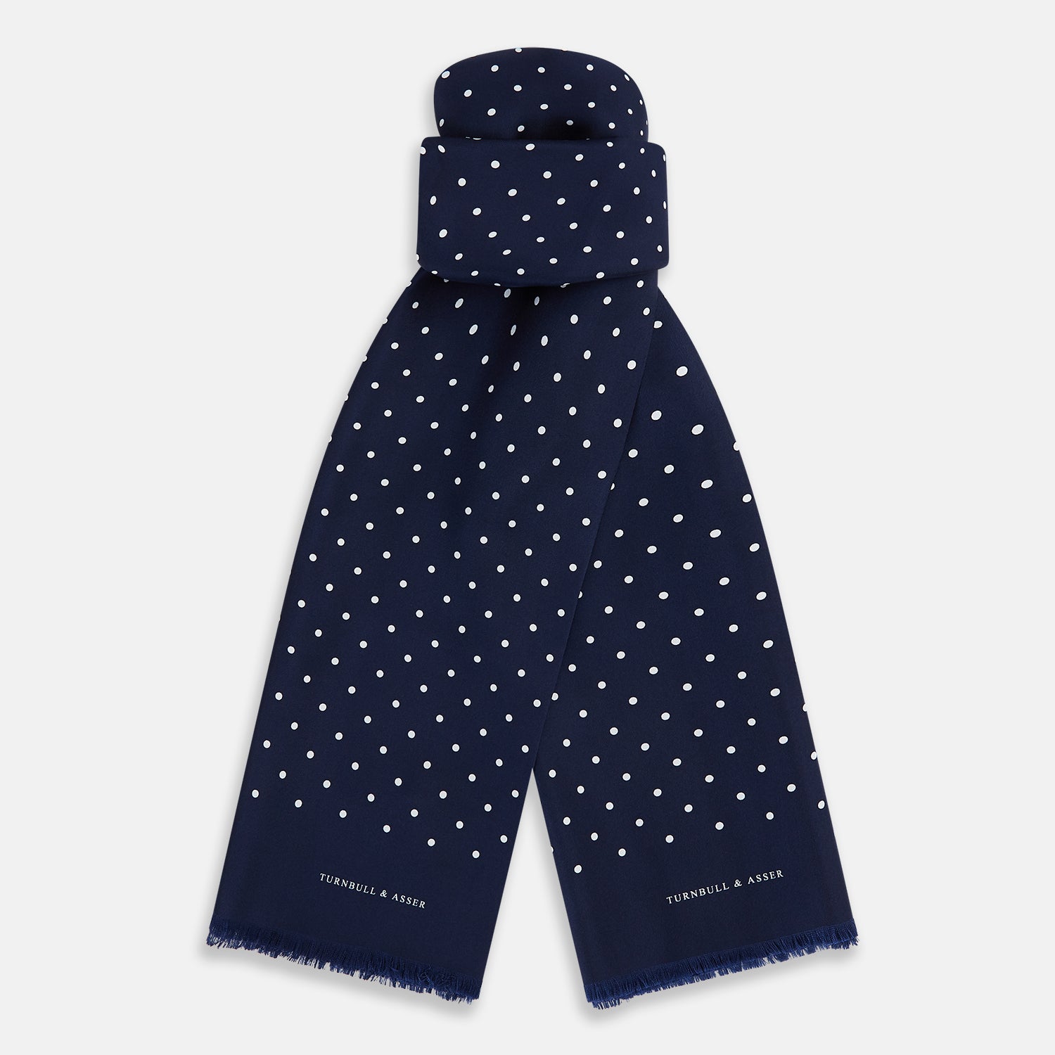 Image 1 of product The Navy and White Spotted Silk Scarf by Turnbull & Asser features white polka dots, a fringed edge, and the brand's name printed near the bottom on both sides. It is neatly folded at the top.