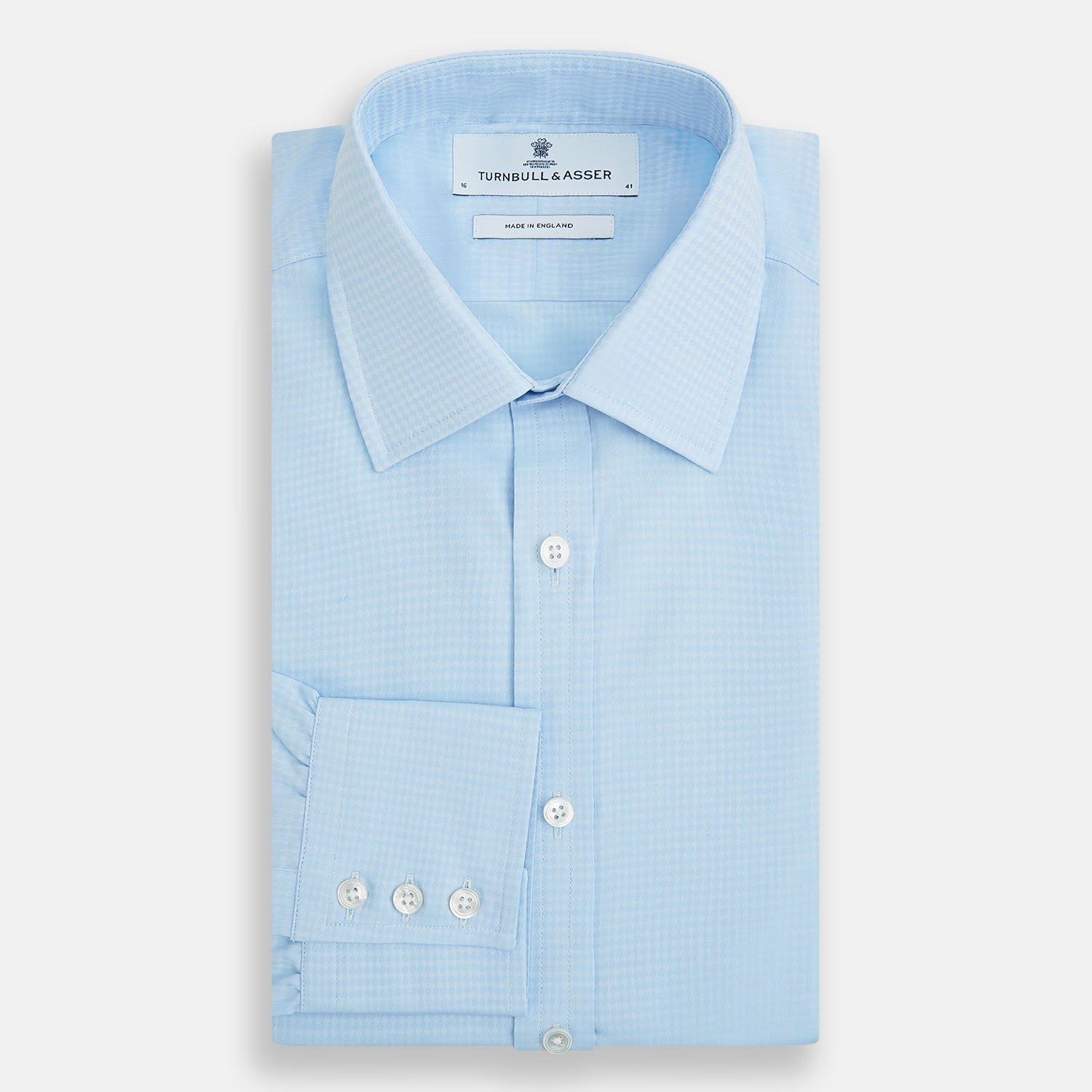 Image 5 of product The Pale Blue Rhombus Mayfair Shirt by Turnbull & Asser features long sleeves, a classic collar, white buttons, and buttoned cuffs, shown laid flat on a white background.
