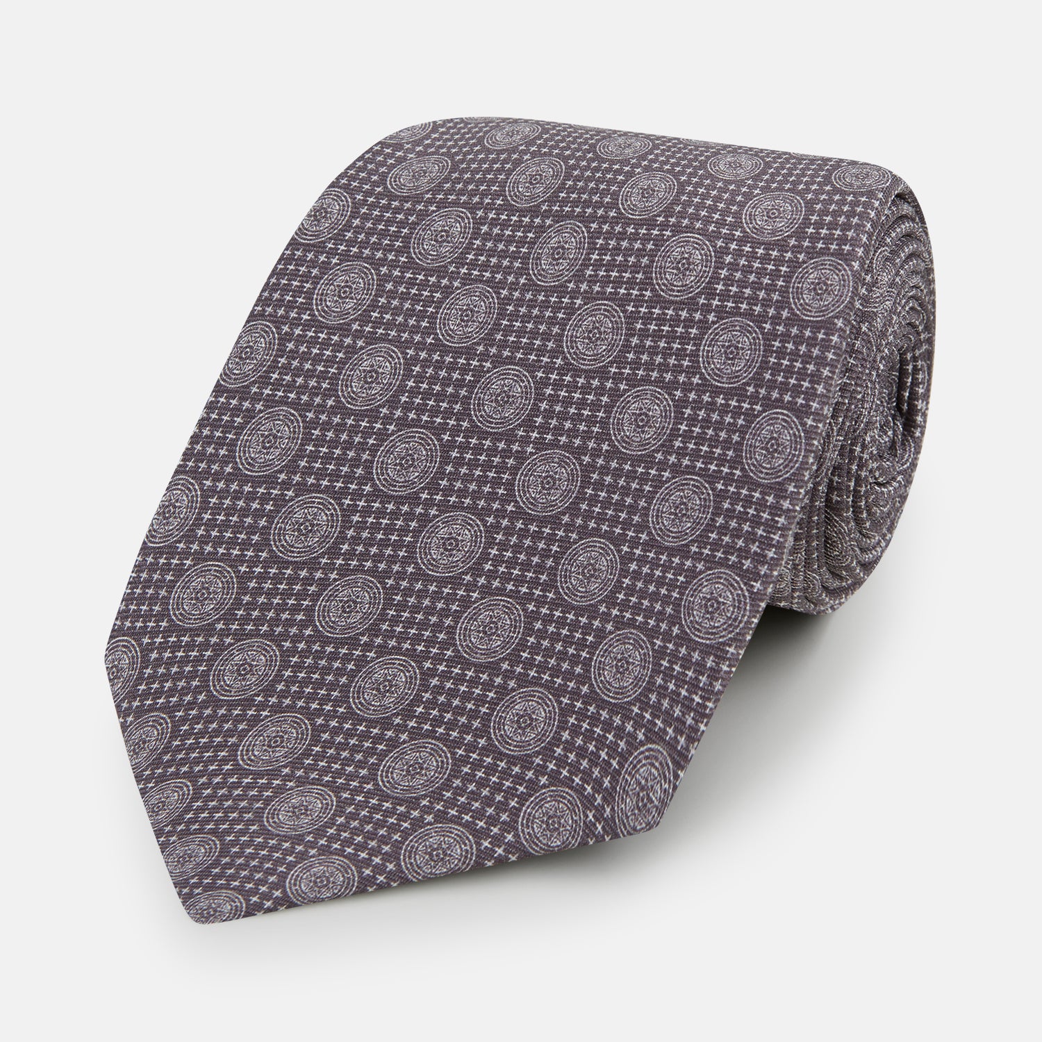 Image 1 of product The Turnbull & Asser Ash Medallion Silk Tie features rolled-up ash silk with gray and light purple medallion and grid-like motifs on a white background.
