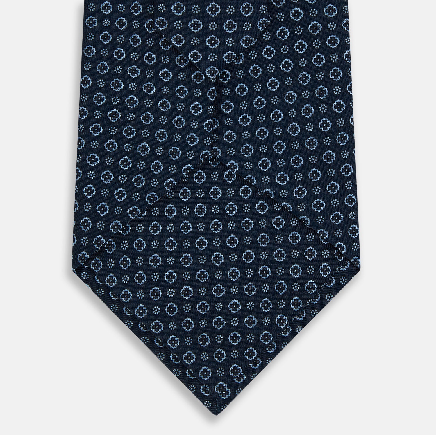 Image 3 of product The Turnbull & Asser Navy Floral Silk Tie is crafted from fine English silk, featuring a repeating pattern of small white circular floral motifs, and is neatly rolled for display against a plain white background.