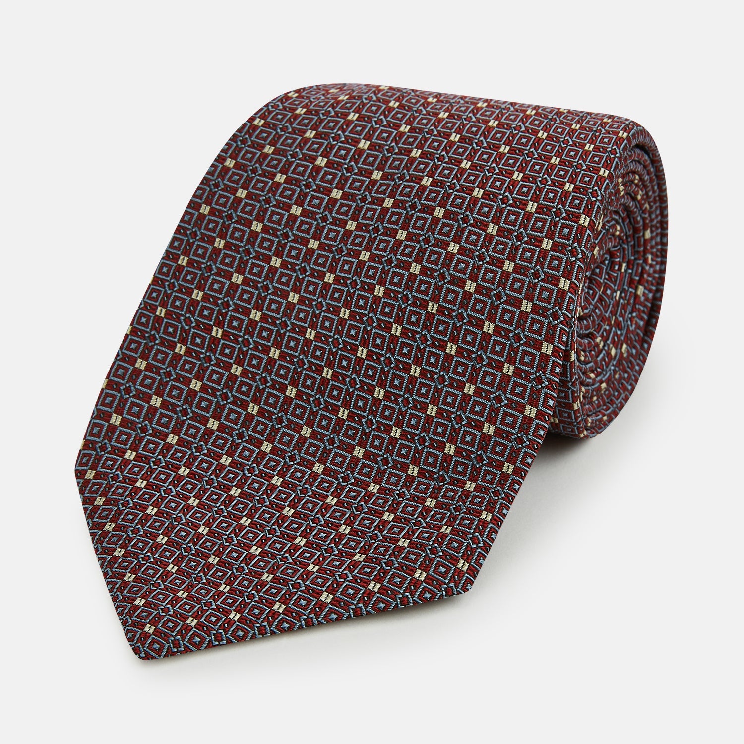 Image 1 of product The Turnbull & Asser Burgundy Geometric Silk Tie, crafted in Britain, features a repeating pattern of light blue and white squares and diamonds. The neatly rolled tie is shown against a plain white background.