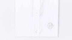 A folded white dress shirt with two visible buttons and a round, gray monogram SRM embroidered near the bottom right side.