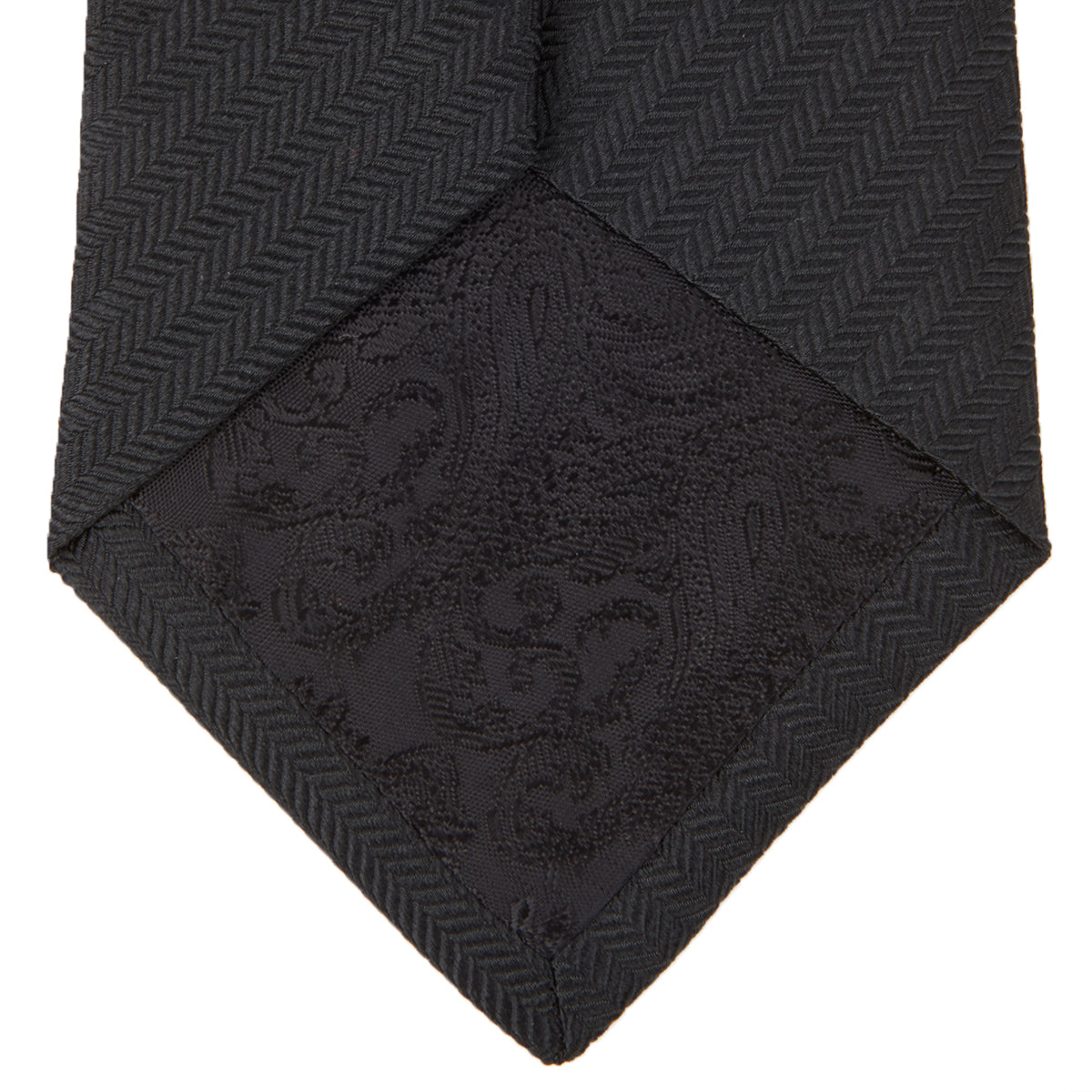 Image 4 of product The Turnbull & Asser Black Herringbone Silk Tie is rolled up and displayed on a plain white background, showcasing its classic style and subtle chevron pattern.