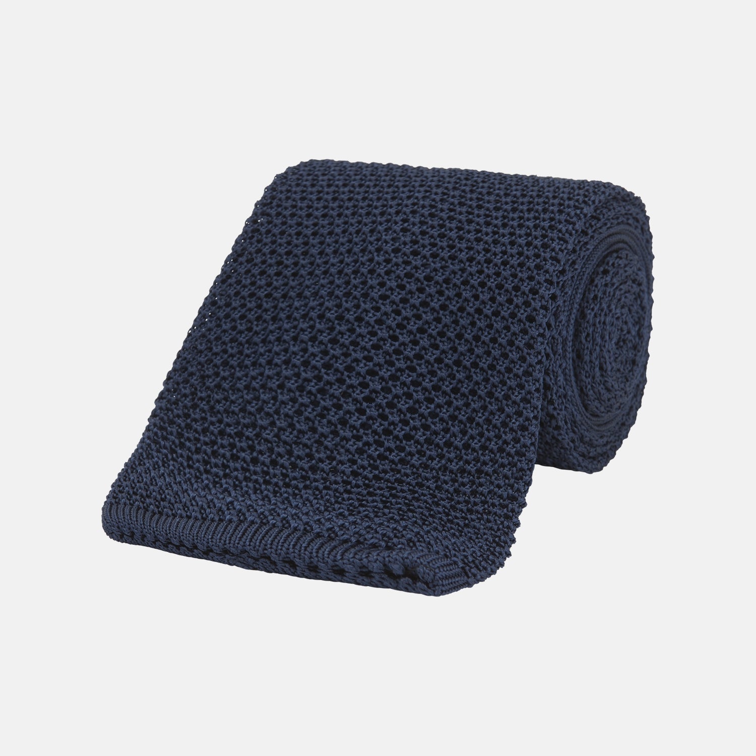 Image 1 of product The Turnbull & Asser Navy Knitted Silk Tie features a textured open weave and flat squared ends, making it a versatile accessory for the modern gentleman’s wardrobe. Shown rolled up on a plain white background.