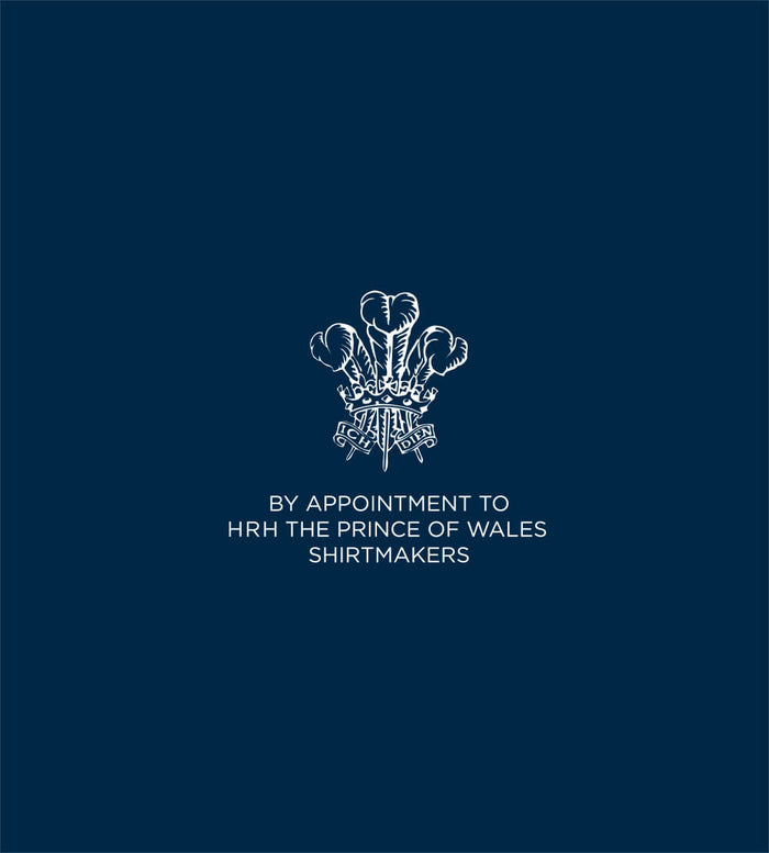 A white emblem with three feathers and a crown above a ribbon is centered on a dark blue background, with the text “BY APPOINTMENT TO HRH THE PRINCE OF WALES SHIRTMAKERS” below it.