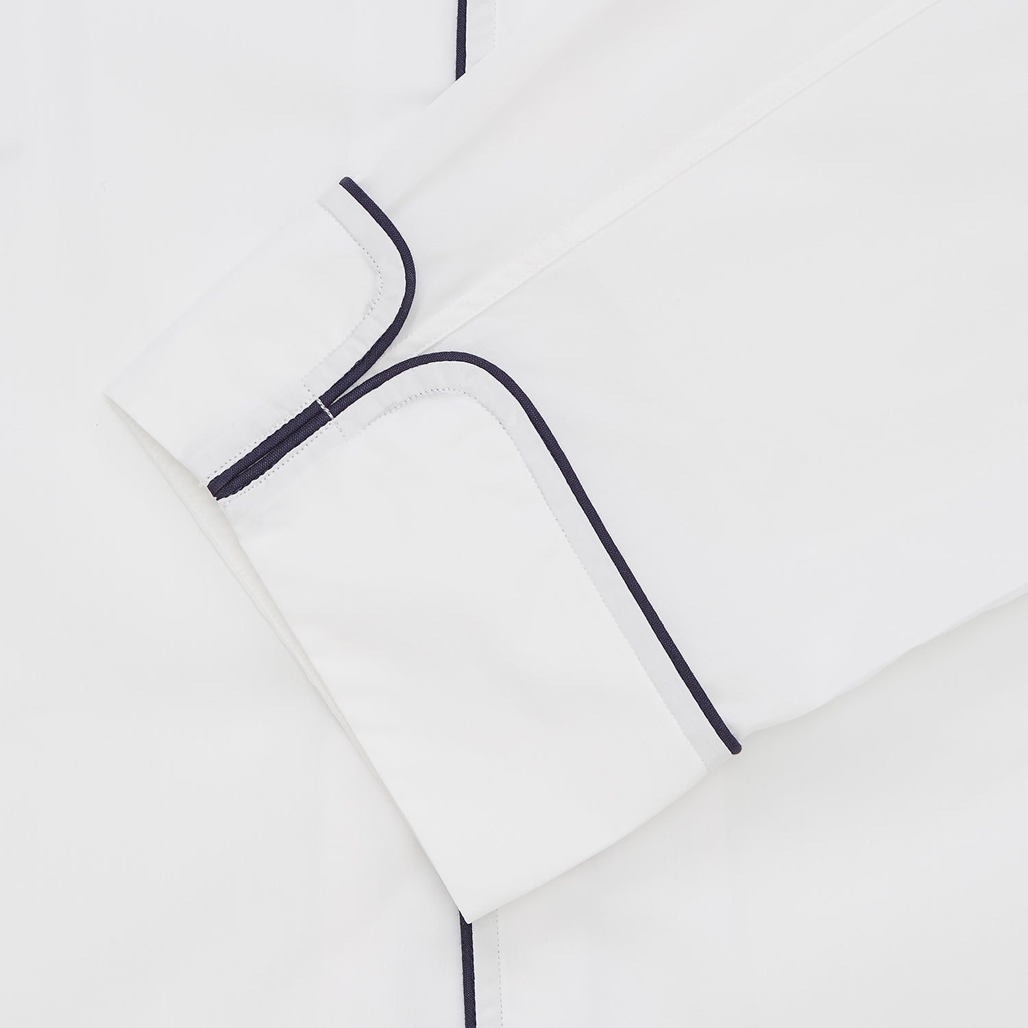 Image 2 of product Turnbull & Asser's White Sea Island Cotton Pyjama Set, featuring a folded white men's top with dark piping and a matching face mask, is showcased on a plain white background.