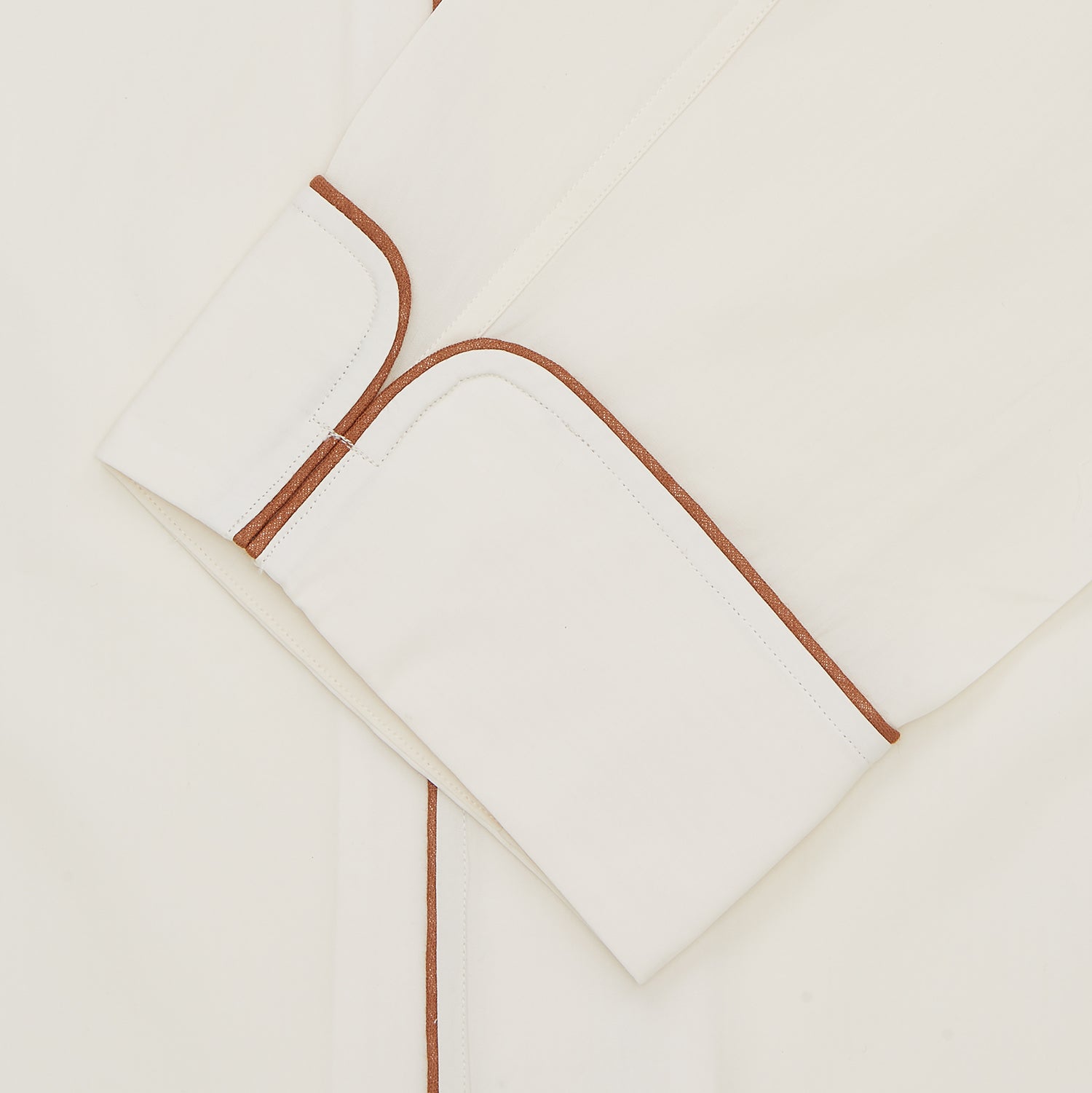 Image 2 of product The Turnbull & Asser Cream Sea Island Cotton Pyjama Set features folded cream pyjamas with brown piping and a matching sleep mask with fabric ties, all elegantly displayed against a plain white background.