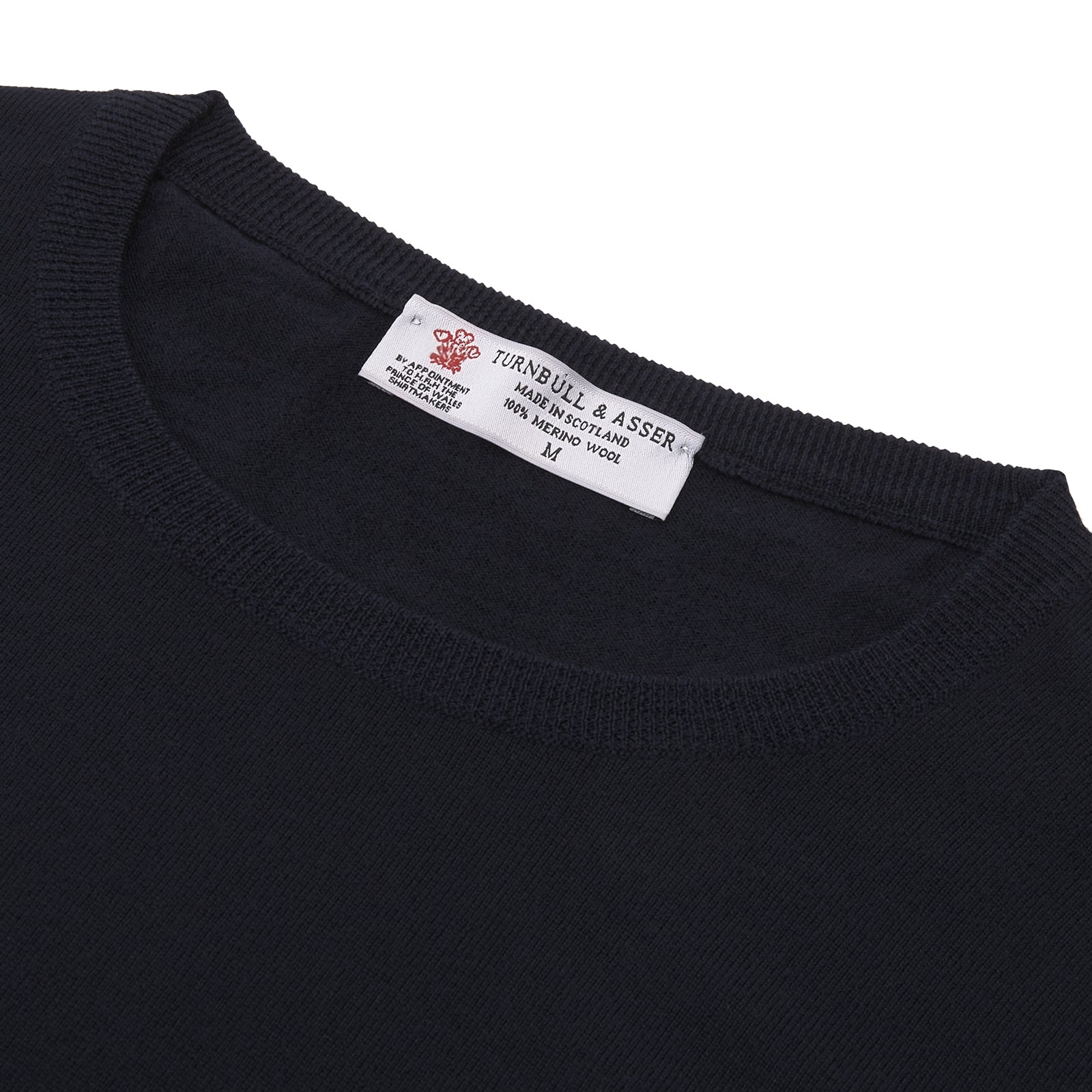 Image 4 of product A neatly folded Indigo Crew Neck Merino Wool Jumper by Turnbull & Asser, featuring a visible brand label at the collar and one sleeve tucked across the front, displayed on a white background—a versatile staple for any gentleman's wardrobe.