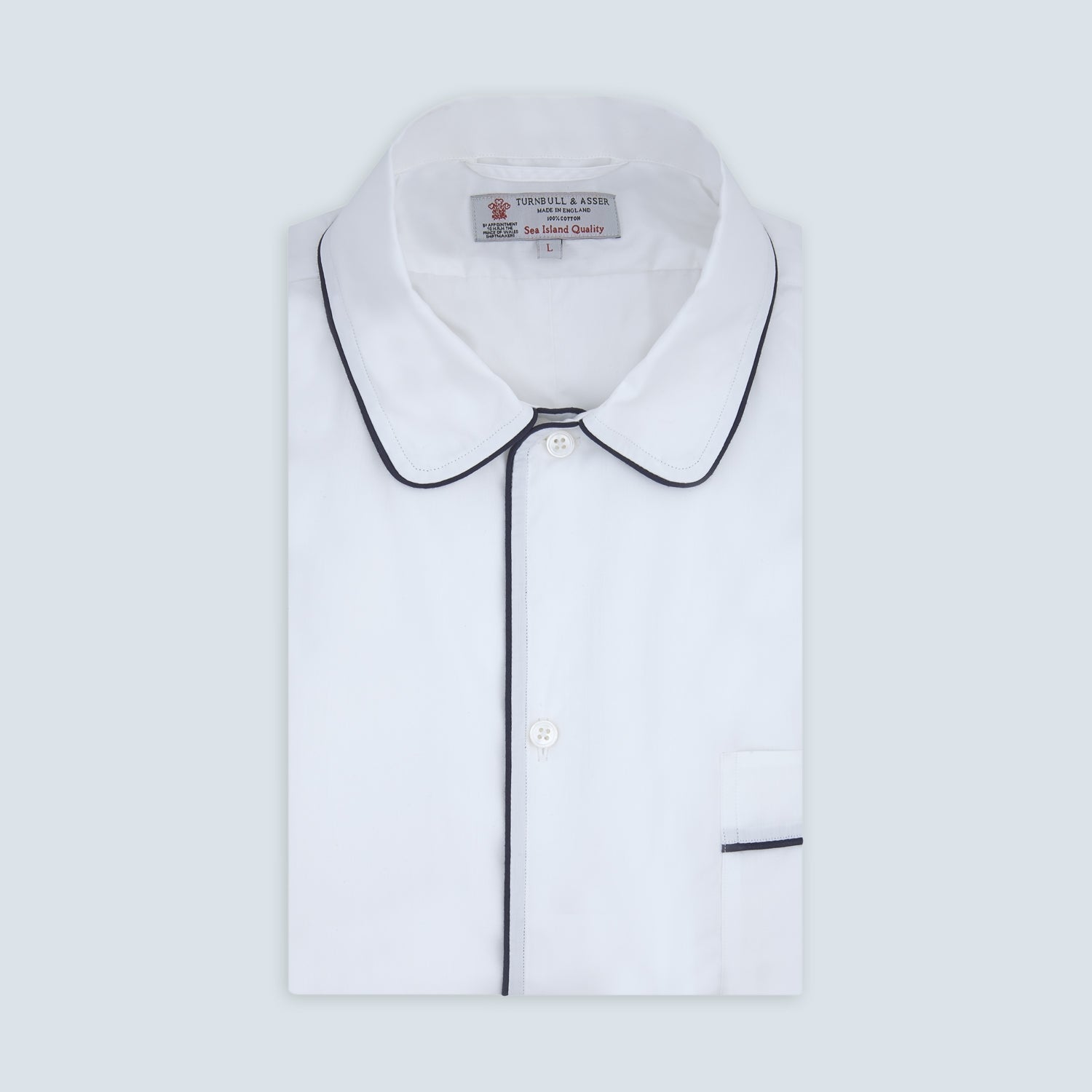 Image 1 of product The Turnbull & Asser White Sea Island Quality Cotton Nightshirt, featuring black piping on the collar and pocket, is elegantly displayed folded against a light grey background.