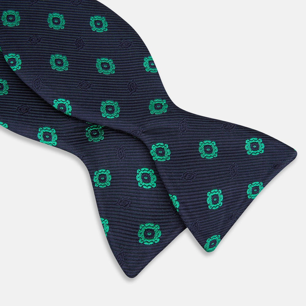 The Navy and Green Motif Silk Bow Tie by Turnbull & Asser features geometric floral patterns, ideal for formalwear, and is shown on a white background.