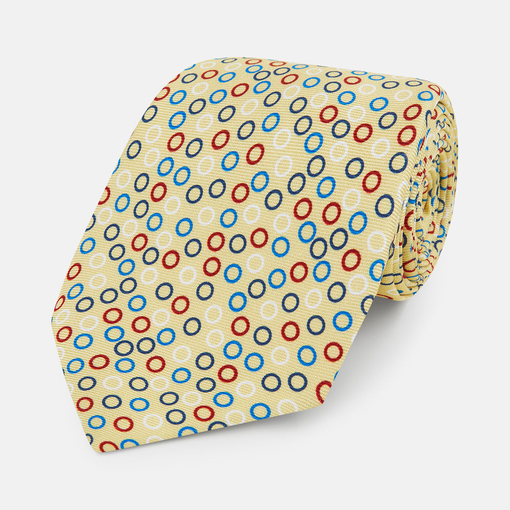 The Turnbull & Asser Multi-coloured Circle Yellow Printed Silk Tie features vibrant blue, red, and black circles evenly spaced across luxurious English silk.