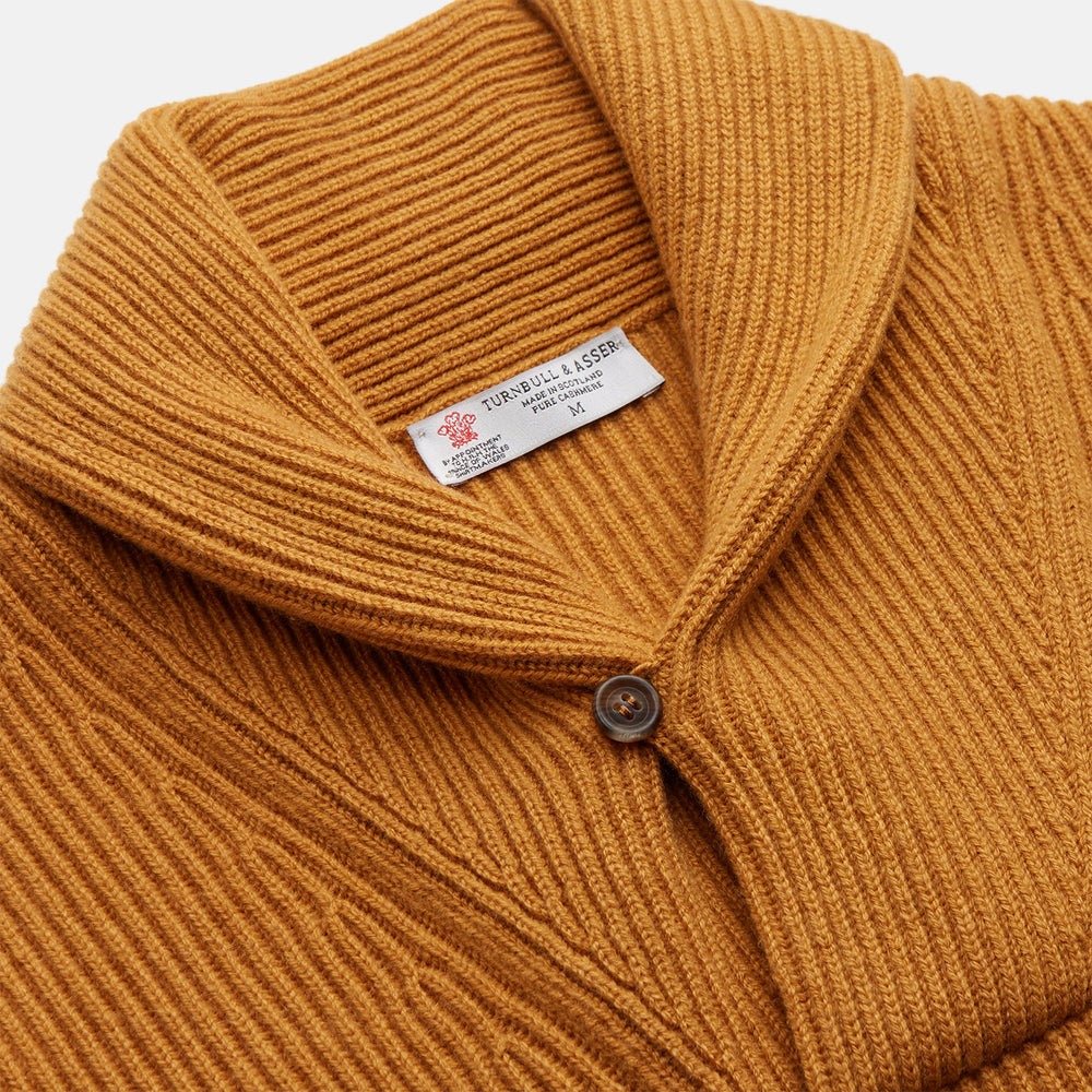 The Turnbull & Asser Gold Cashmere Shawl Neck Lytton Jumper, in ribbed knit with a horn button at the neckline, is stylishly laid flat on a white background.