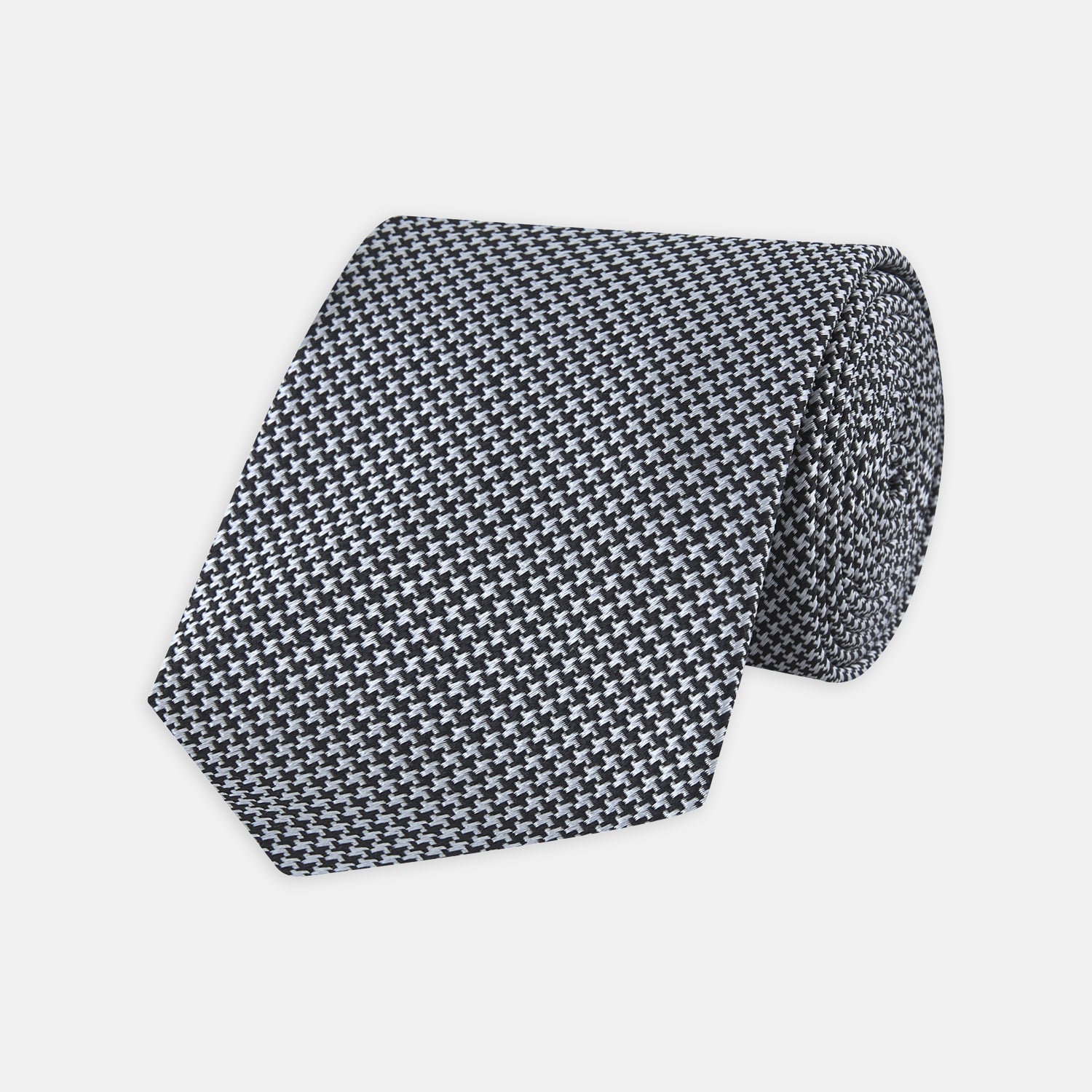 View 1 of product The Turnbull & Asser White and Black Houndstooth Woven Silk Tie, shown rolled on a light grey background, adds a classic touch to any smart outfit.