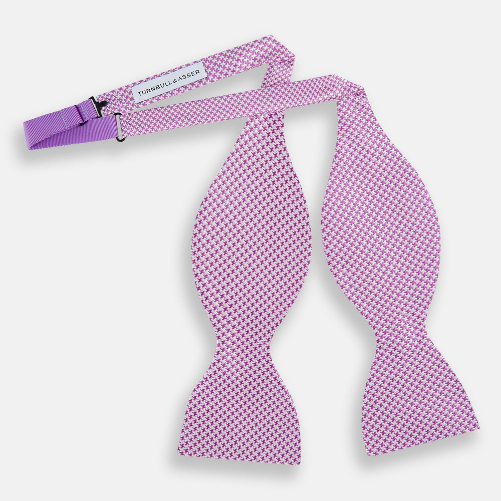 The Turnbull & Asser Pink and White Houndstooth Silk Bow Tie is shown against a plain white background, making it a stylish choice for formalwear.