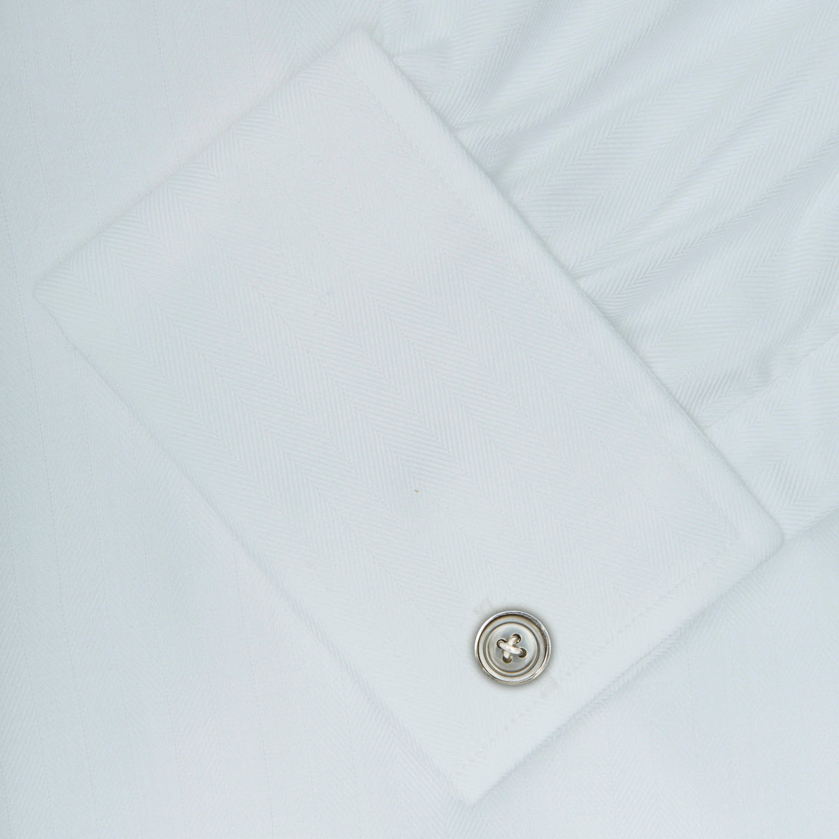 View 6 of product The Turnbull & Asser White Herringbone Superfine Cotton Shirt features a T&A collar, double cuffs, and a visible label inside the collar, shown neatly folded on a light blue background—ideal for minimalist looks or pairing with bold ties.