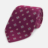 View 1 of product The Turnbull & Asser Purple Motif Silk Tie, rolled up and displayed on a light gray background, features small blue and white geometric designs—an elegant British touch for any formal event.
