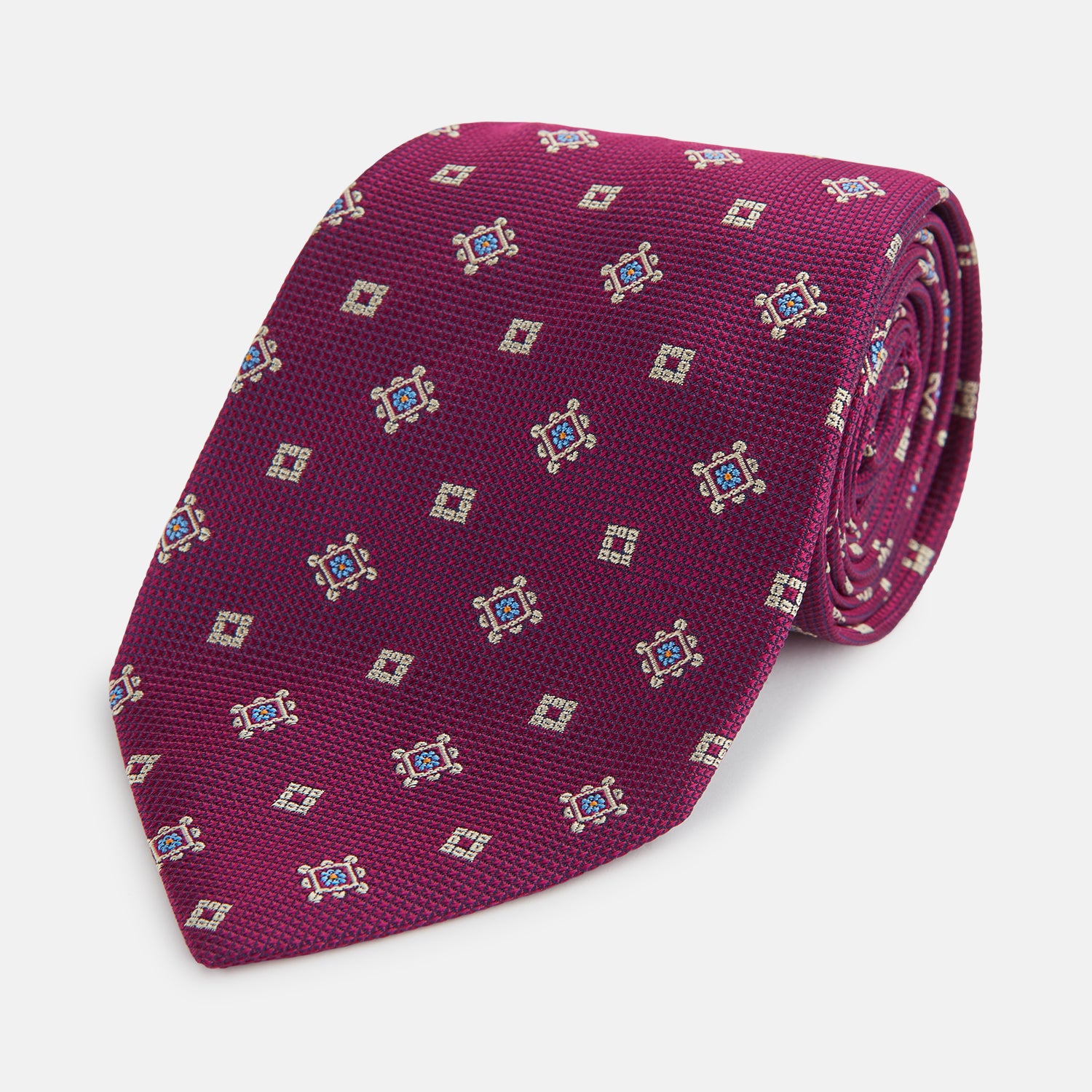 View 1 of product The Turnbull & Asser Purple Motif Silk Tie, rolled up and displayed on a light gray background, features small blue and white geometric designs—an elegant British touch for any formal event.