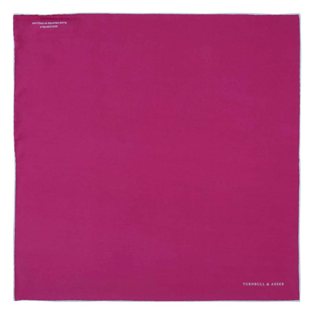 The Fuchsia and White Piped Silk Pocket Square by Turnbull & Asser features white edges and the brand’s name printed in white in the bottom right corner—a timeless men’s accessory.