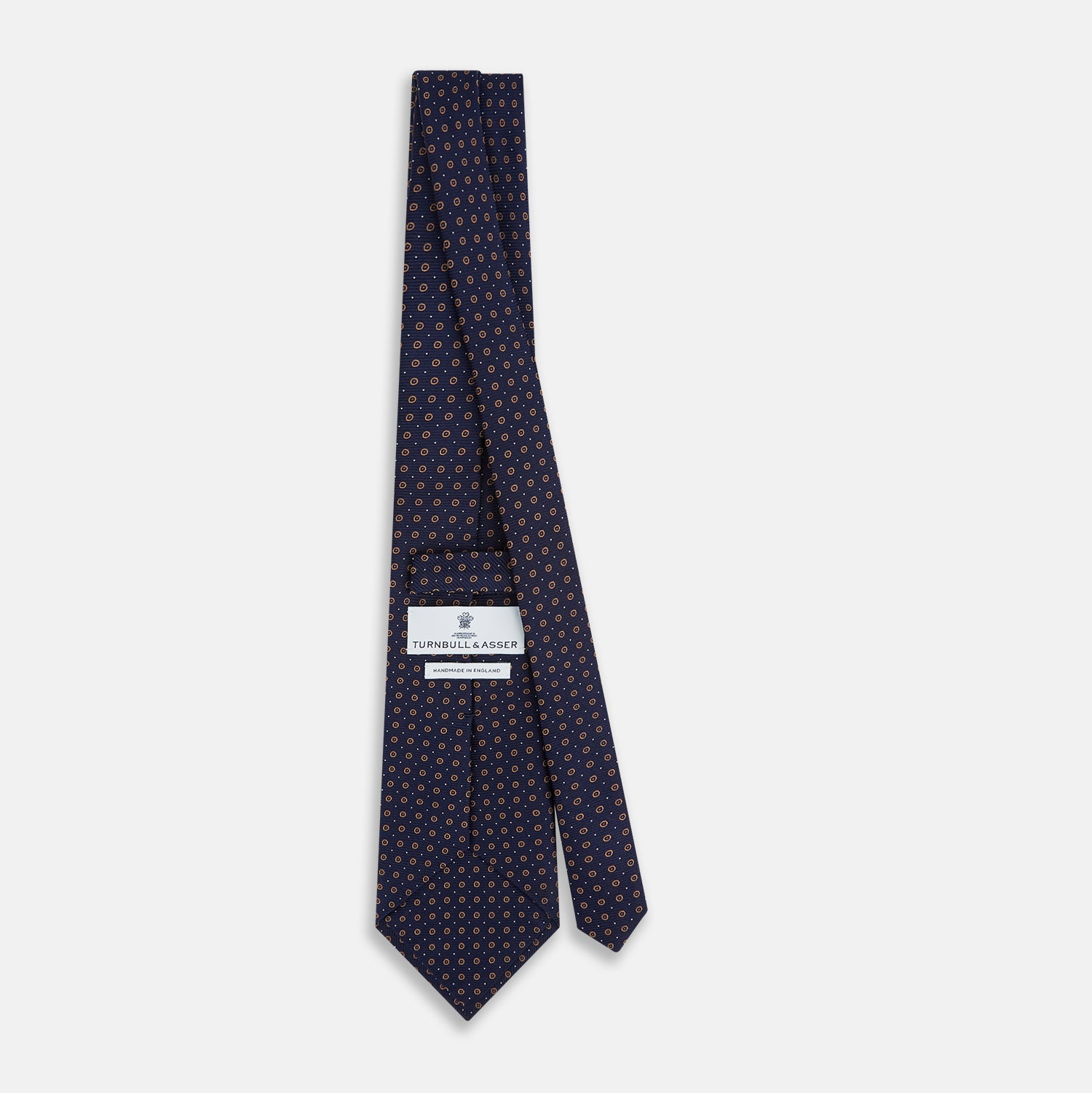 View 4 of product The Turnbull & Asser Navy and Grey Circle Silk Tie, featuring a refined pattern of evenly spaced circles, is elegantly displayed rolled up on a white background—an excellent option for modern office wear.